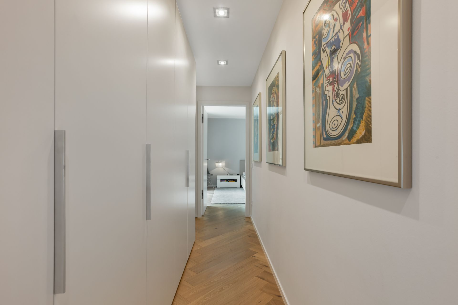 Schmaler Flur mit weißen Einbauschränken und zwei bunten Bildern an der Wand.