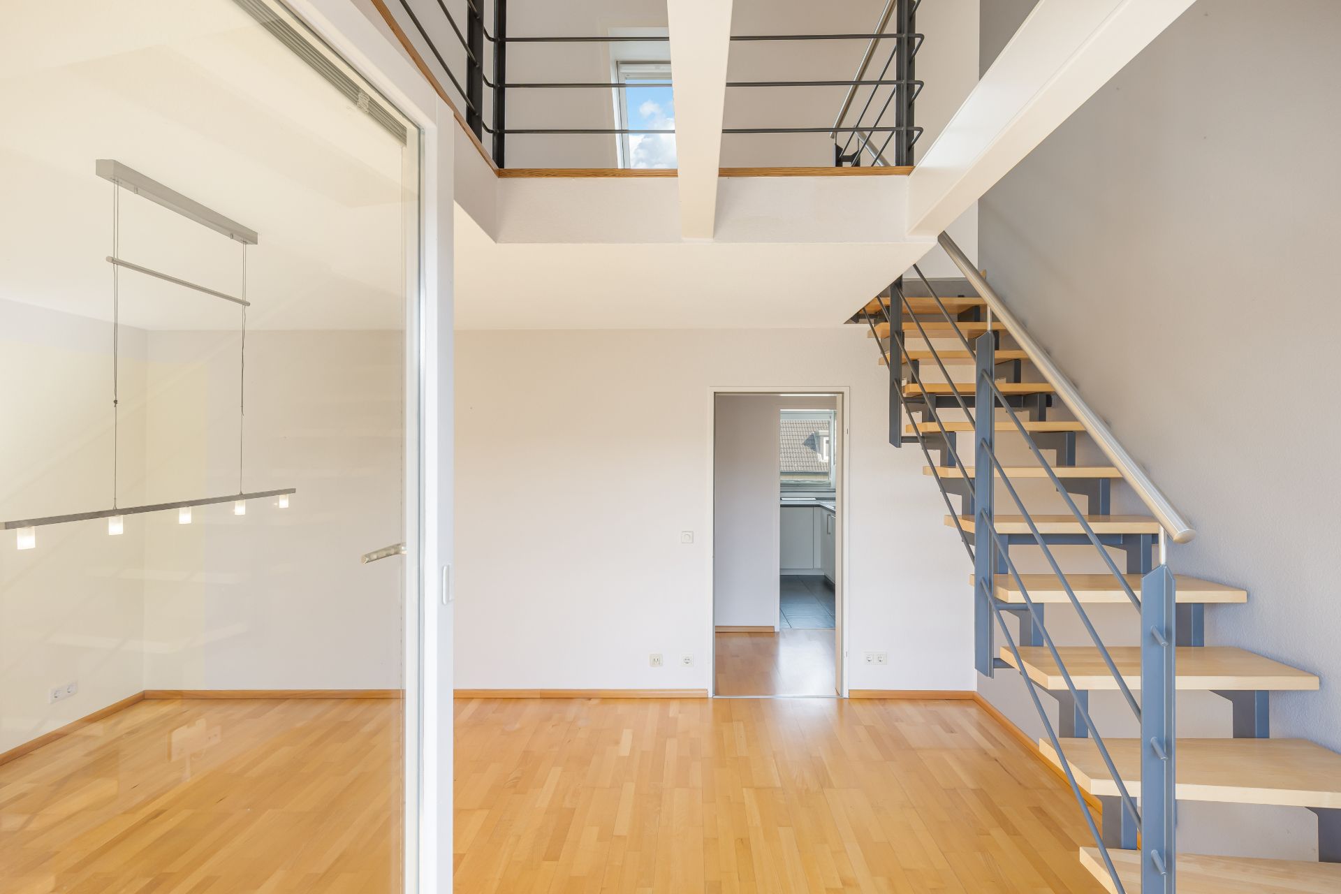 Helles Wohnzimmer mit Holztreppe und offener Galerie, Parkettboden und Sicht auf angrenzenden Raum.