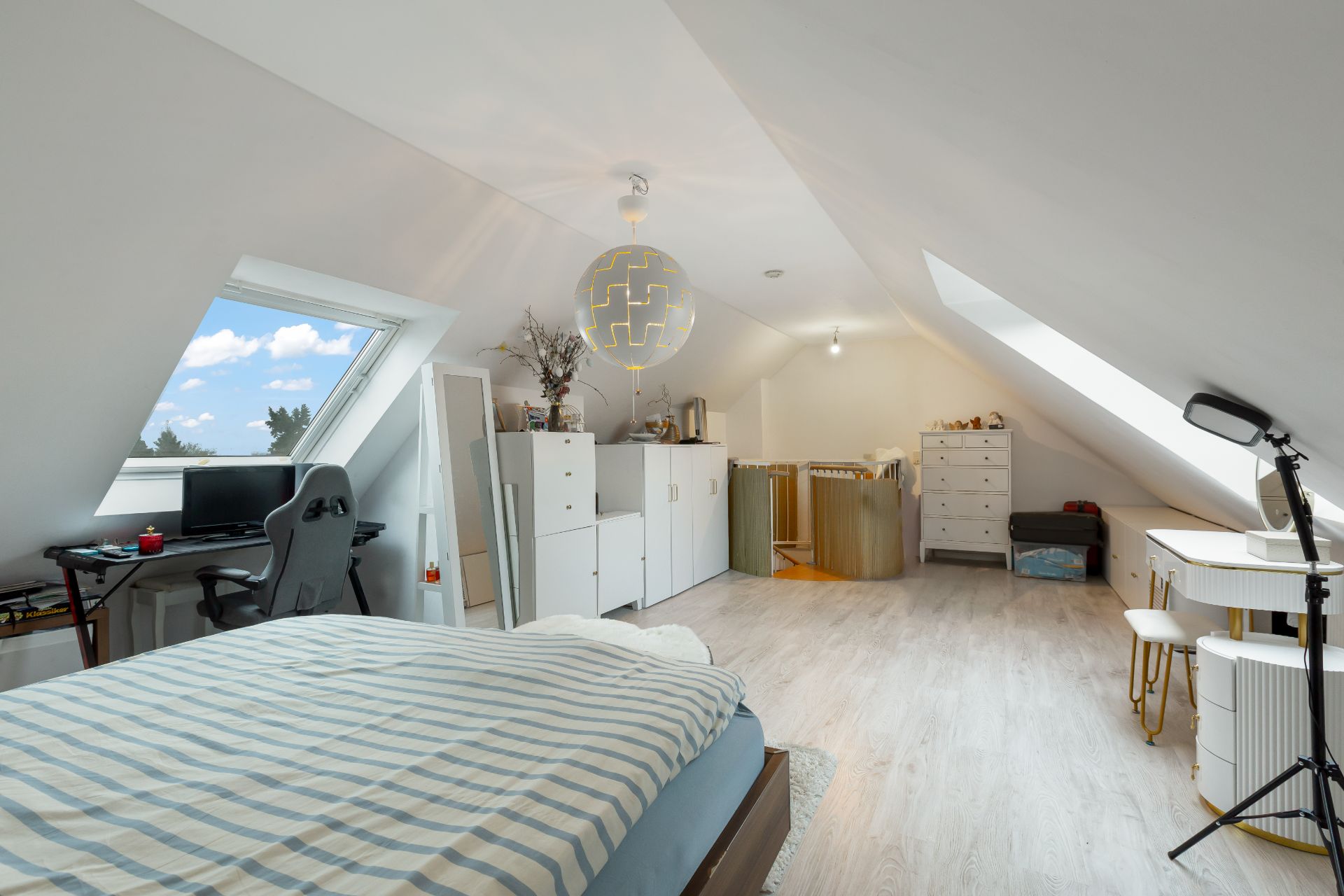 Helles Dachzimmer mit Bett, Schreibtisch, Kommode und großen Dachfenstern.
