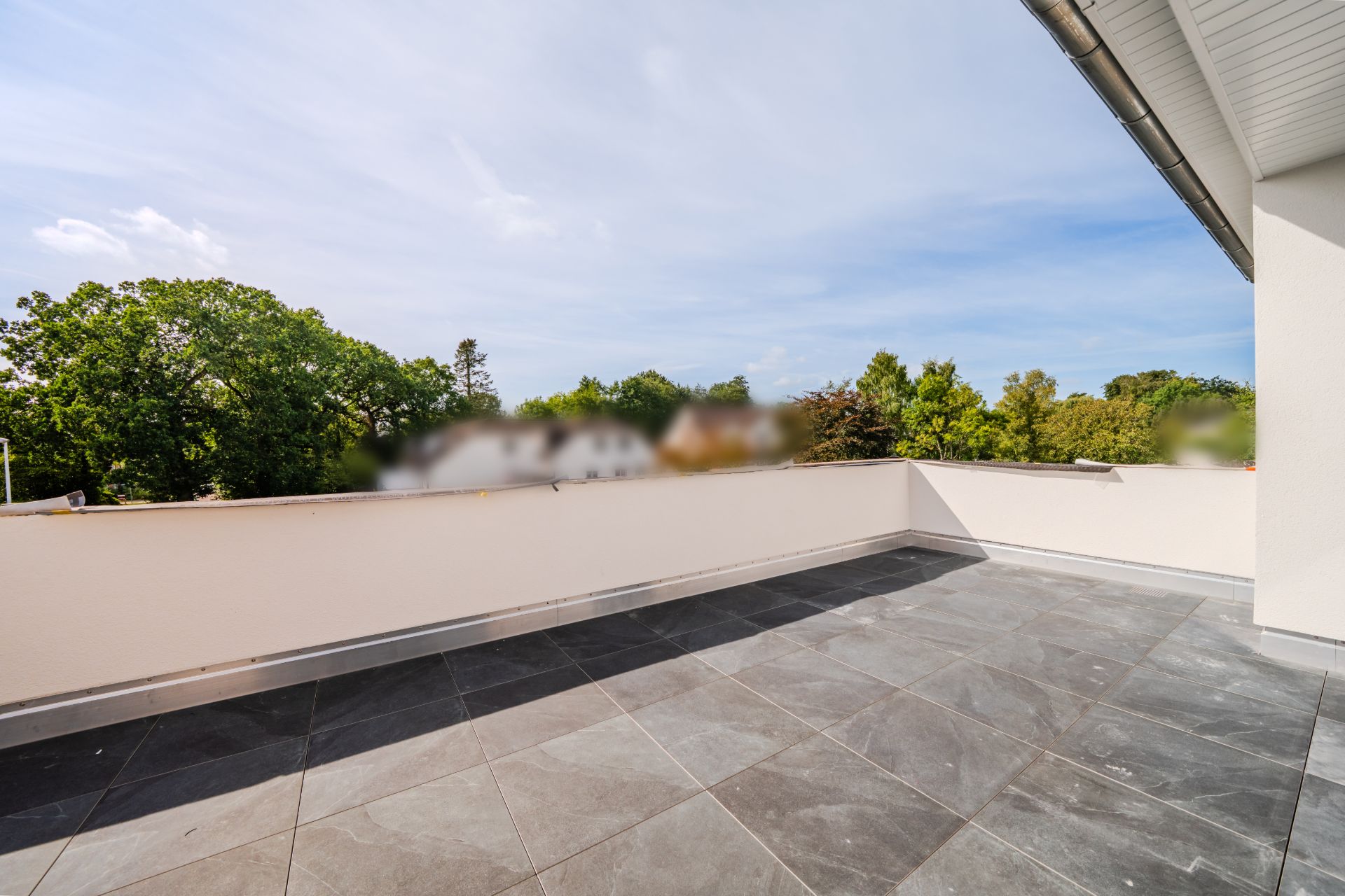 Große Dachterrasse mit grauen Fliesen und Blick auf Bäume.