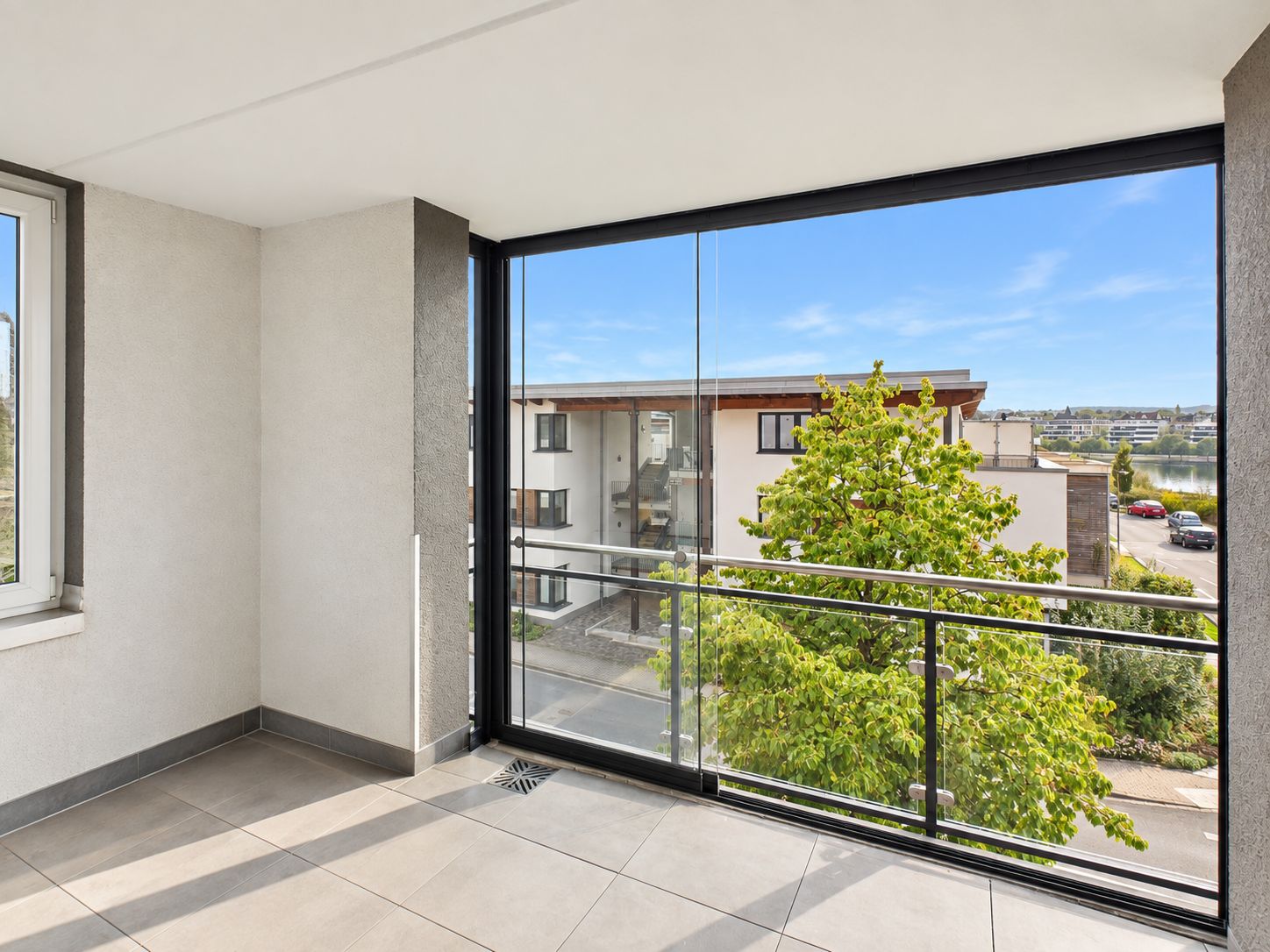 Überdachter Balkon mit Glasgeländer und Blick auf Baum und Wohngebäude.