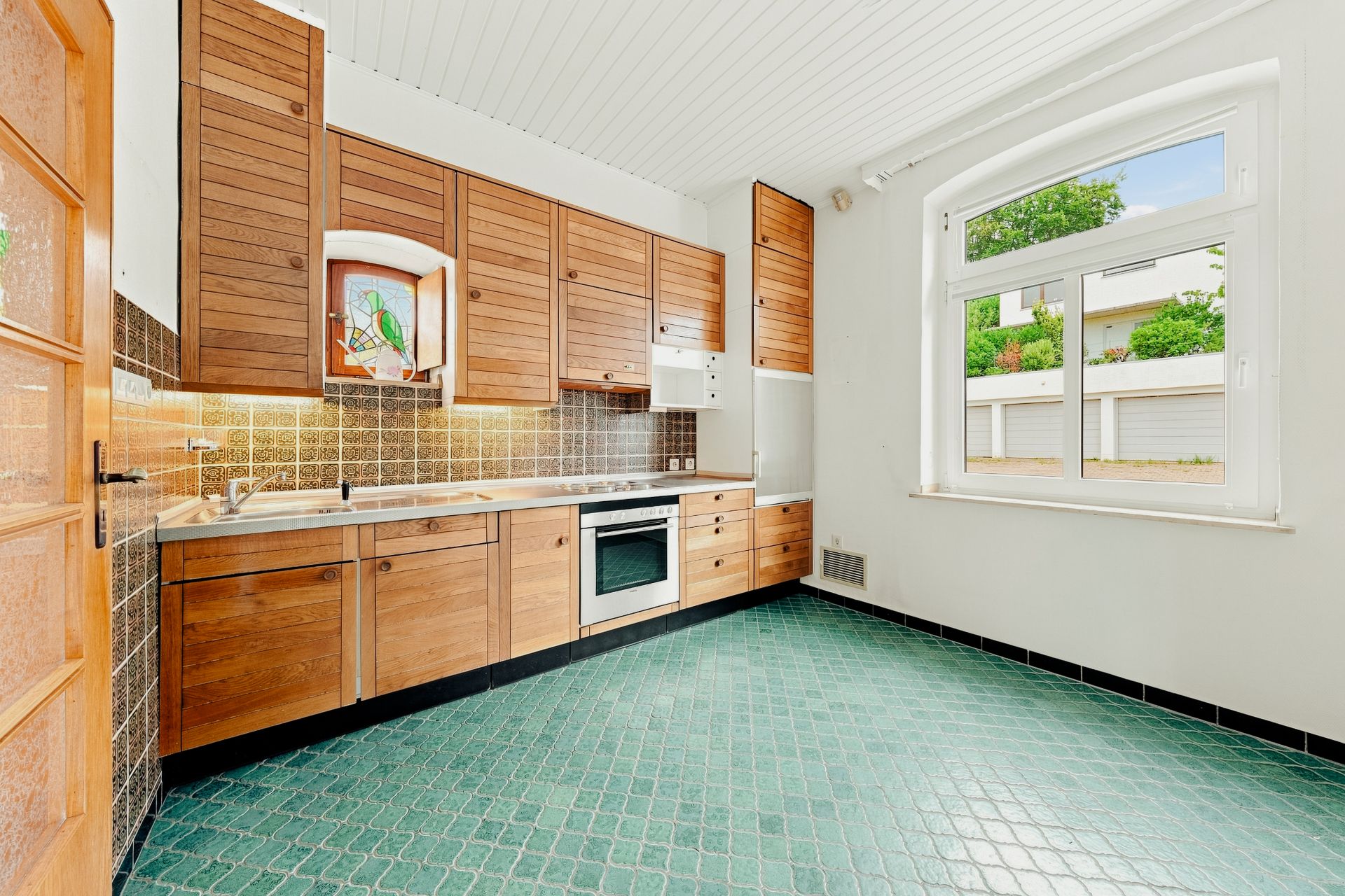 Helle Küche mit Holzschränken, grünem Fliesenboden und großem Fenster.