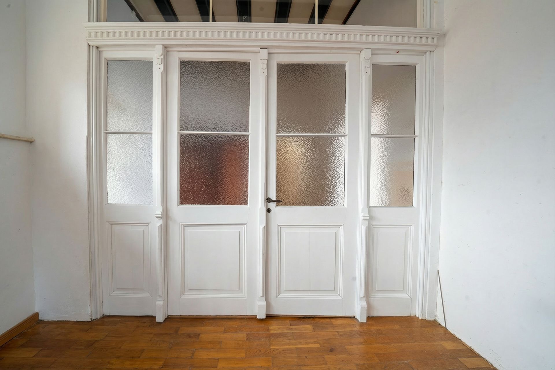 Weiße Doppeltür mit Milchglas und Holzrahmen in einem Raum mit Parkettboden.