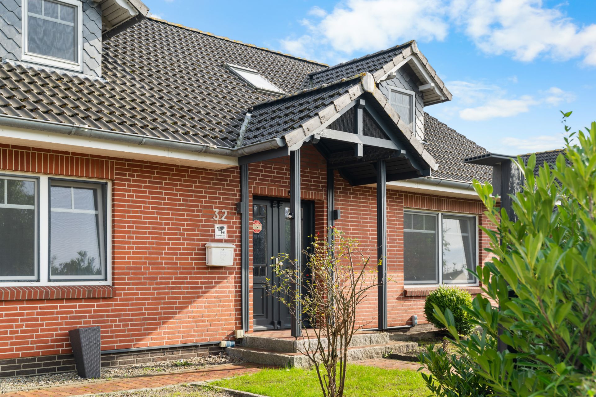 Vorderansicht eines Backsteinhauses mit dunkelgrauer Eingangstür und kleinen Garten vor dem Haus.