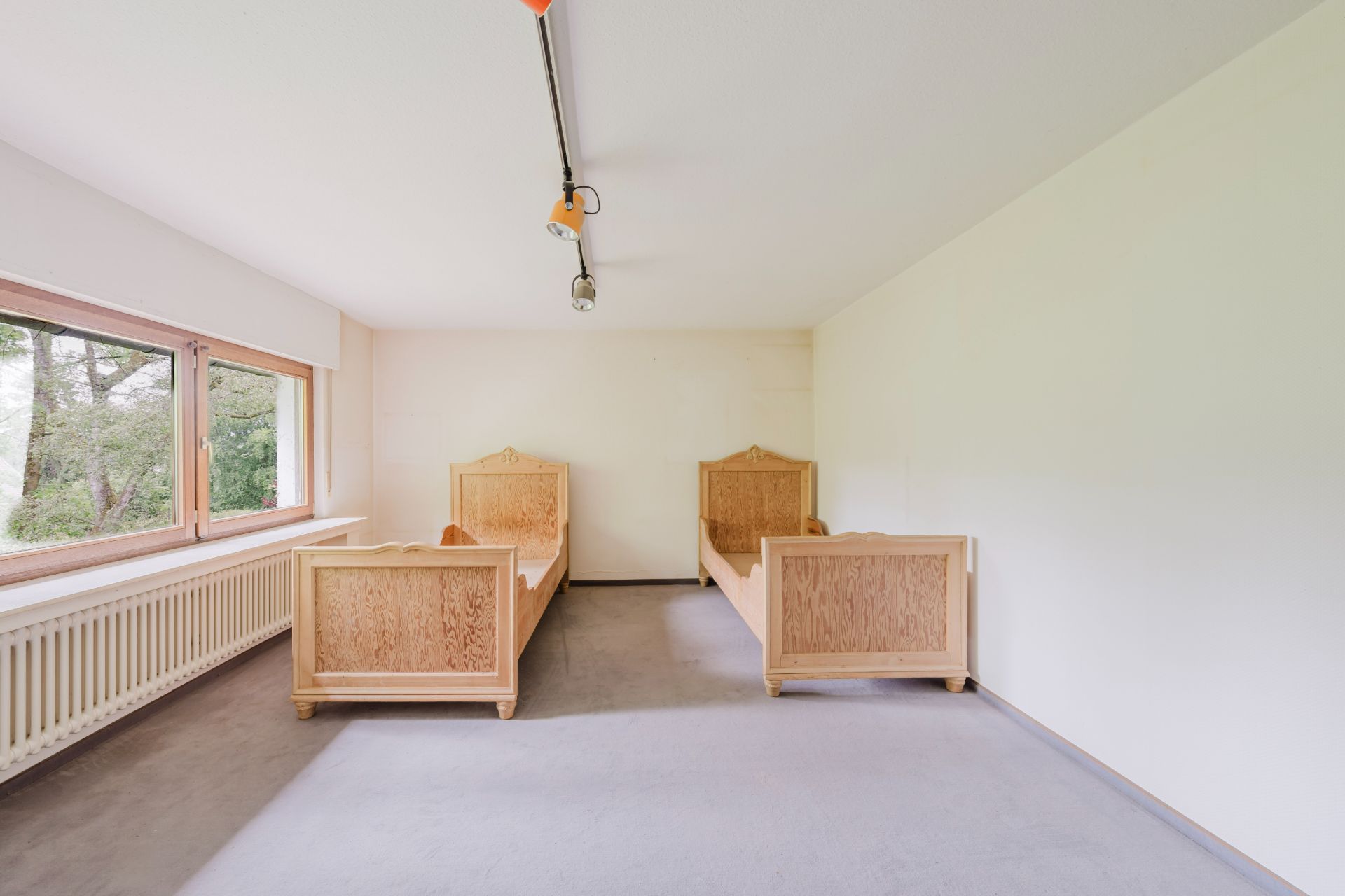Zimmer mit zwei einzelnen Holzbetten, großem Fenster und weiß gestrichenen Wänden.