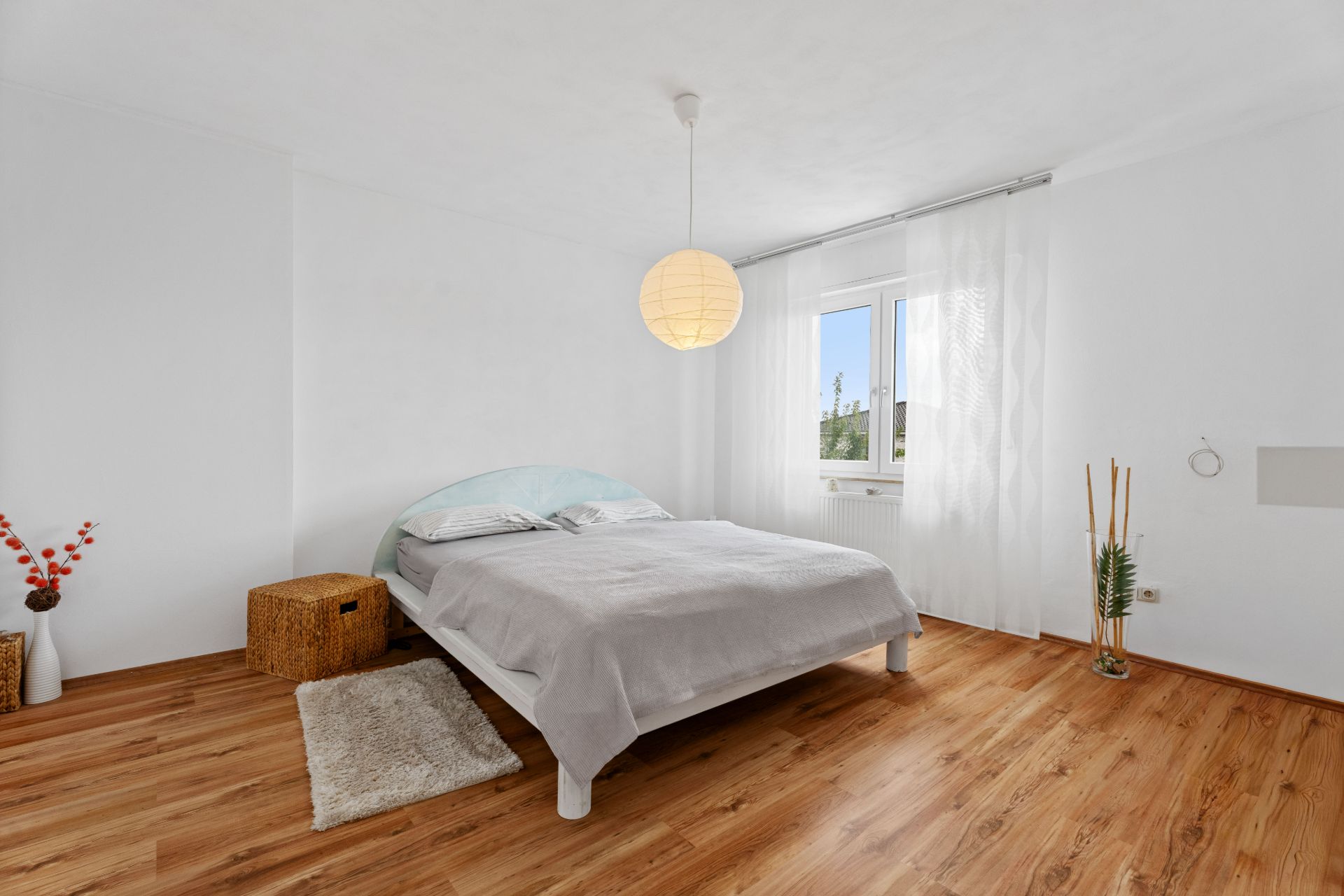 Helles Schlafzimmer mit Doppelbett, Holzboden, Fenster und minimaler Dekoration.