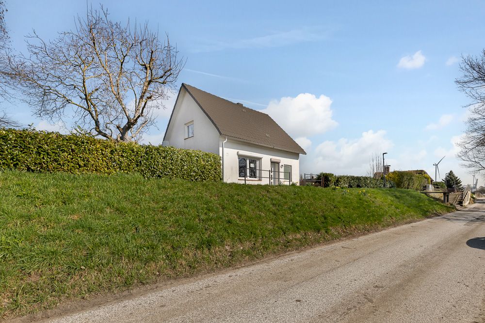 Weißes Einfamilienhaus mit Satteldach hinter einer Hecke, an einer ruhigen Straße gelegen.