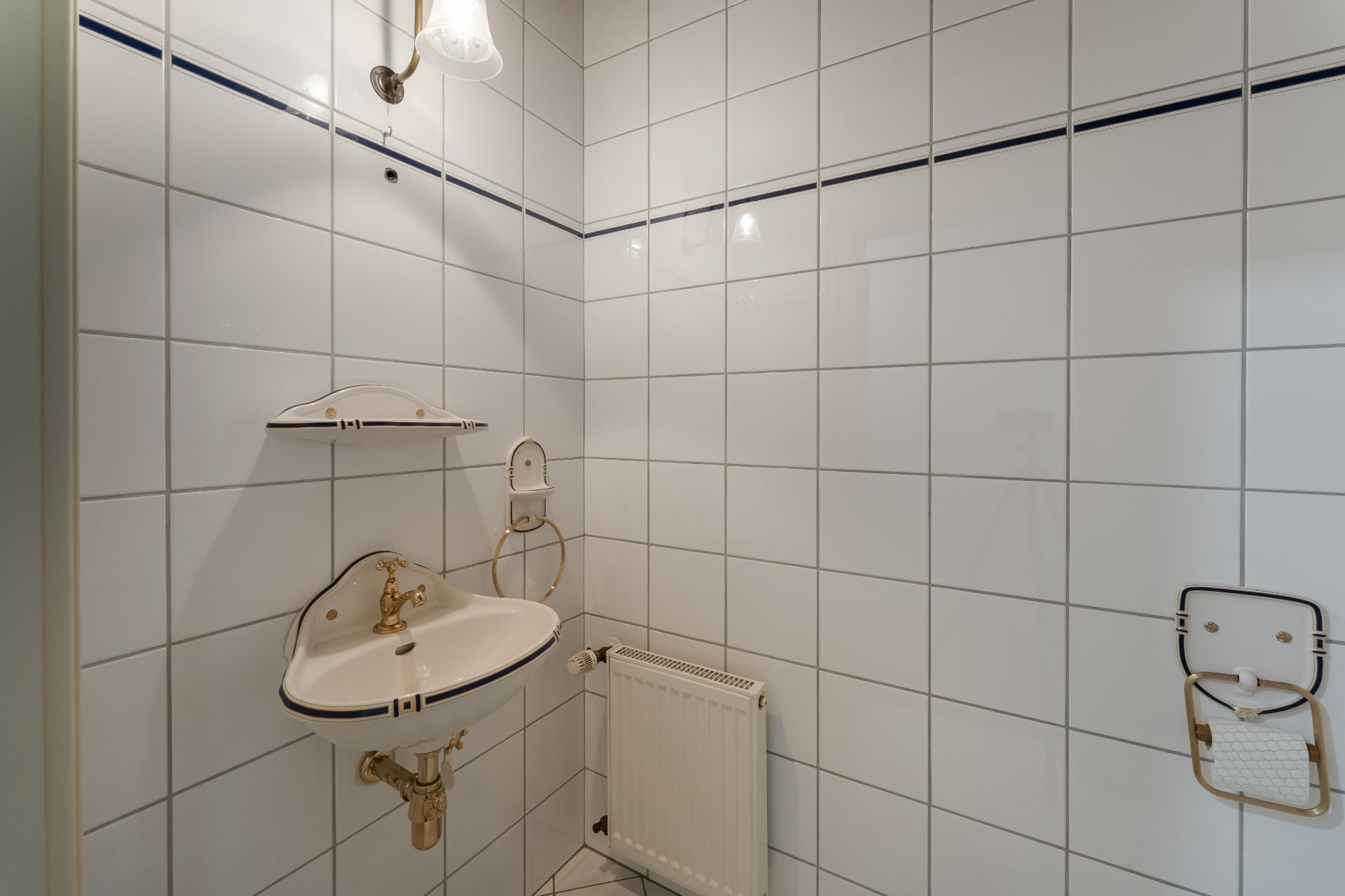 Ecke eines Badezimmers mit weiß gefliesten Wänden, kleinem Waschbecken und Heizkörper.