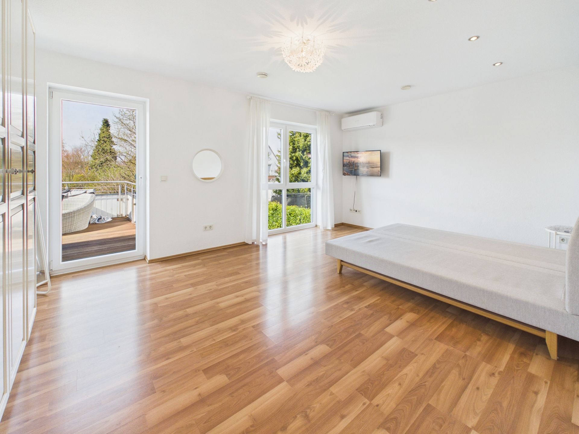 Helles Wohnzimmer mit Parkettboden, Sofa, Balkonzugang und großem Fenster.