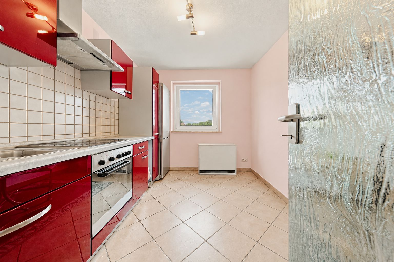 Moderne Küche mit roten Schränken, Backofen, Kühlschrank und Fenster mit Ausblick.