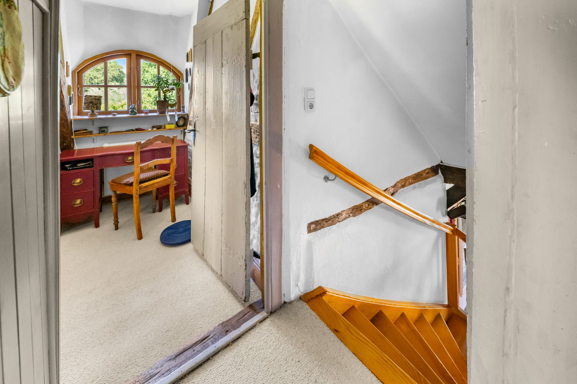 Raum mit Schreibtisch und Stuhl, daneben Treppe mit Holzstufen und weißer Wand.