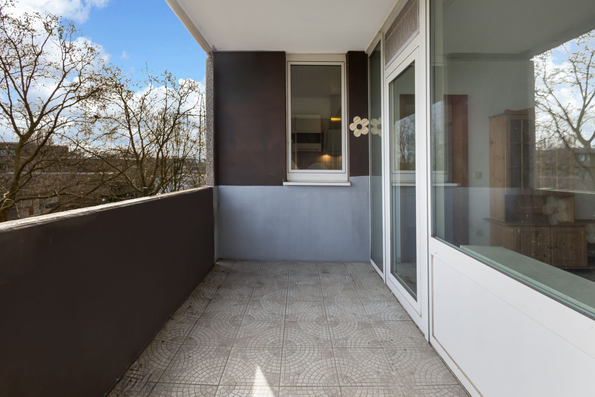 Überdachter Balkon mit Fliesenboden, Glasbrüstung und Blick auf Bäume.