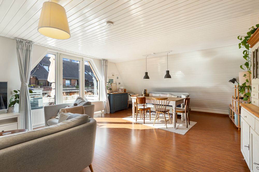 Helles Wohnzimmer mit Sofa, Esstisch, großen Fenstern und Holzboden.
