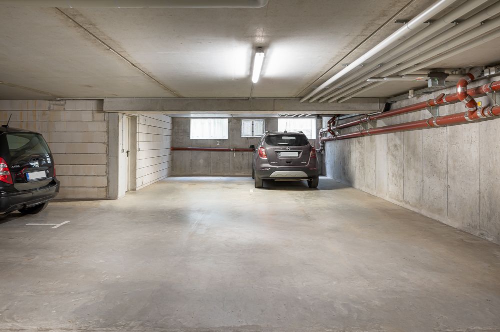 Unterirdische Garage mit zwei geparkten Autos, Betonwänden und sichtbaren Rohrleitungen.