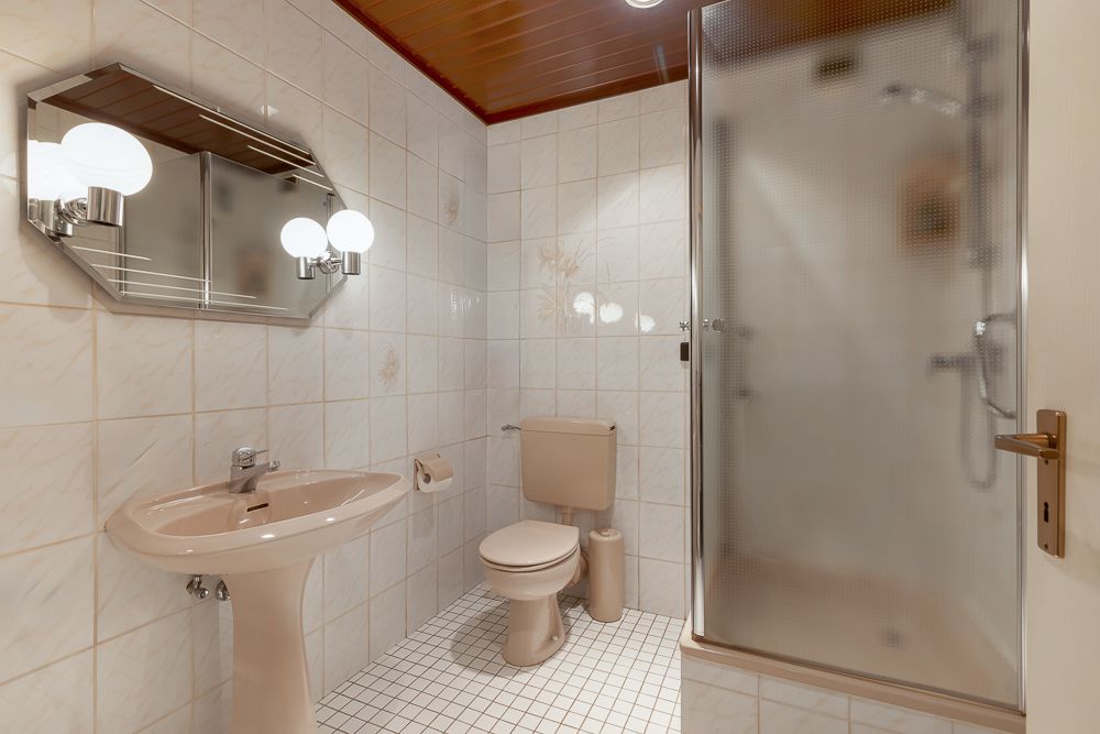 Badezimmer mit Waschbecken, Spiegel, Toilette und Duschkabine mit Milchglas-Tür.