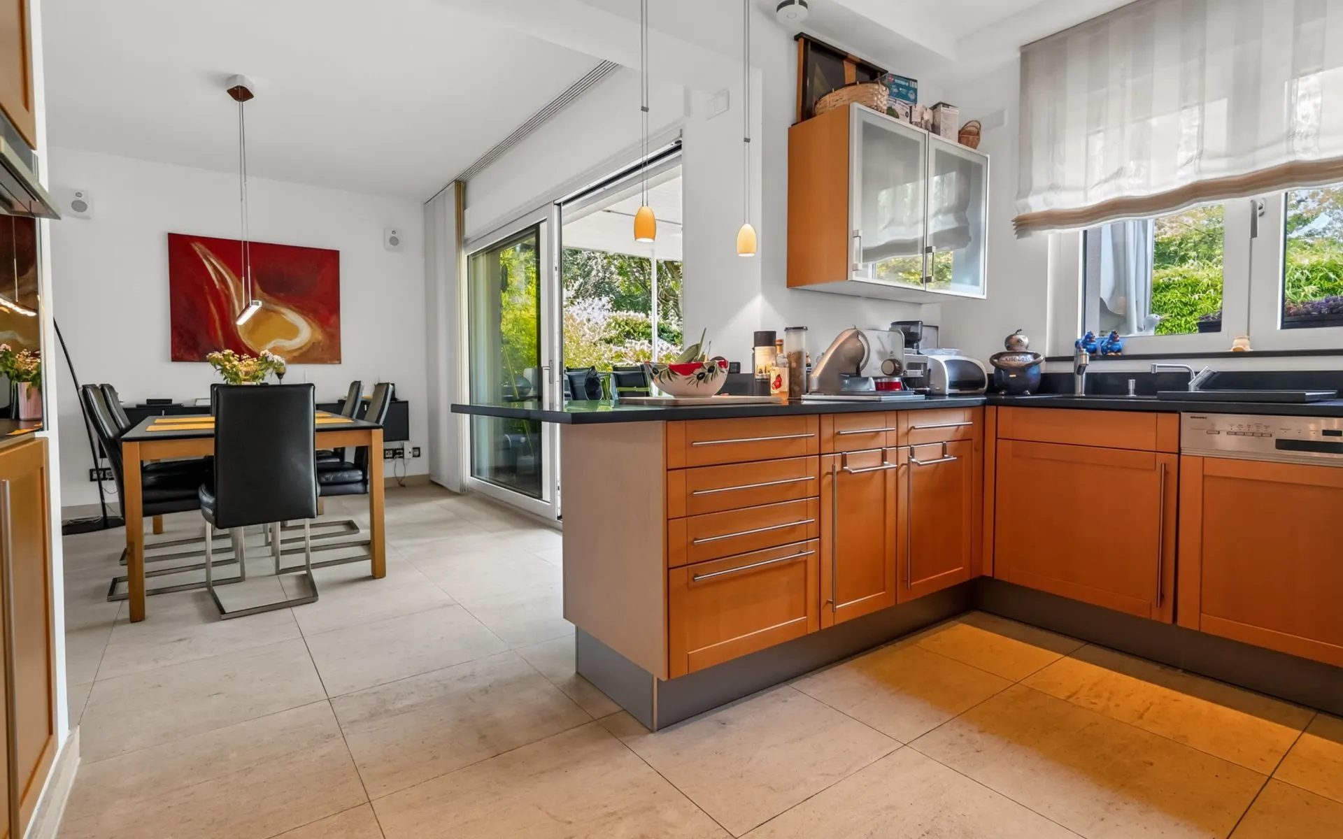 Moderne Küche mit Holzschränken und Essbereich, große Fenster und Blick in den Garten.