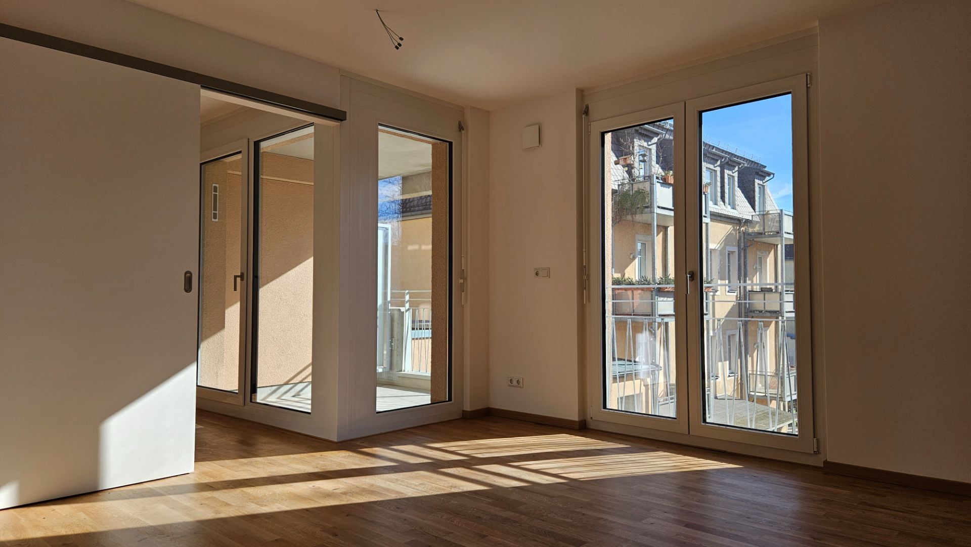 Helles Wohnzimmer mit Holzboden, großen Fenstern und Zugang zum Balkon.