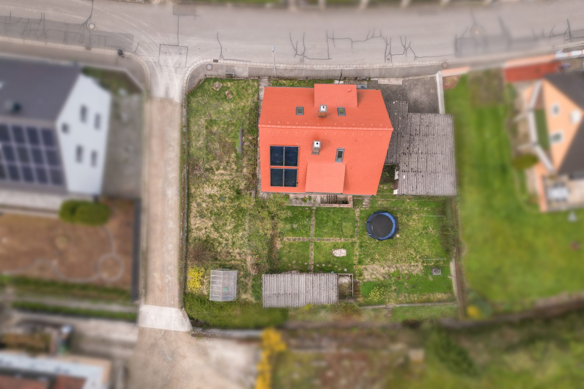 Luftaufnahme eines Hauses mit rotem Dach, Solarpaneelen, Garten und kleinem Trampolin.