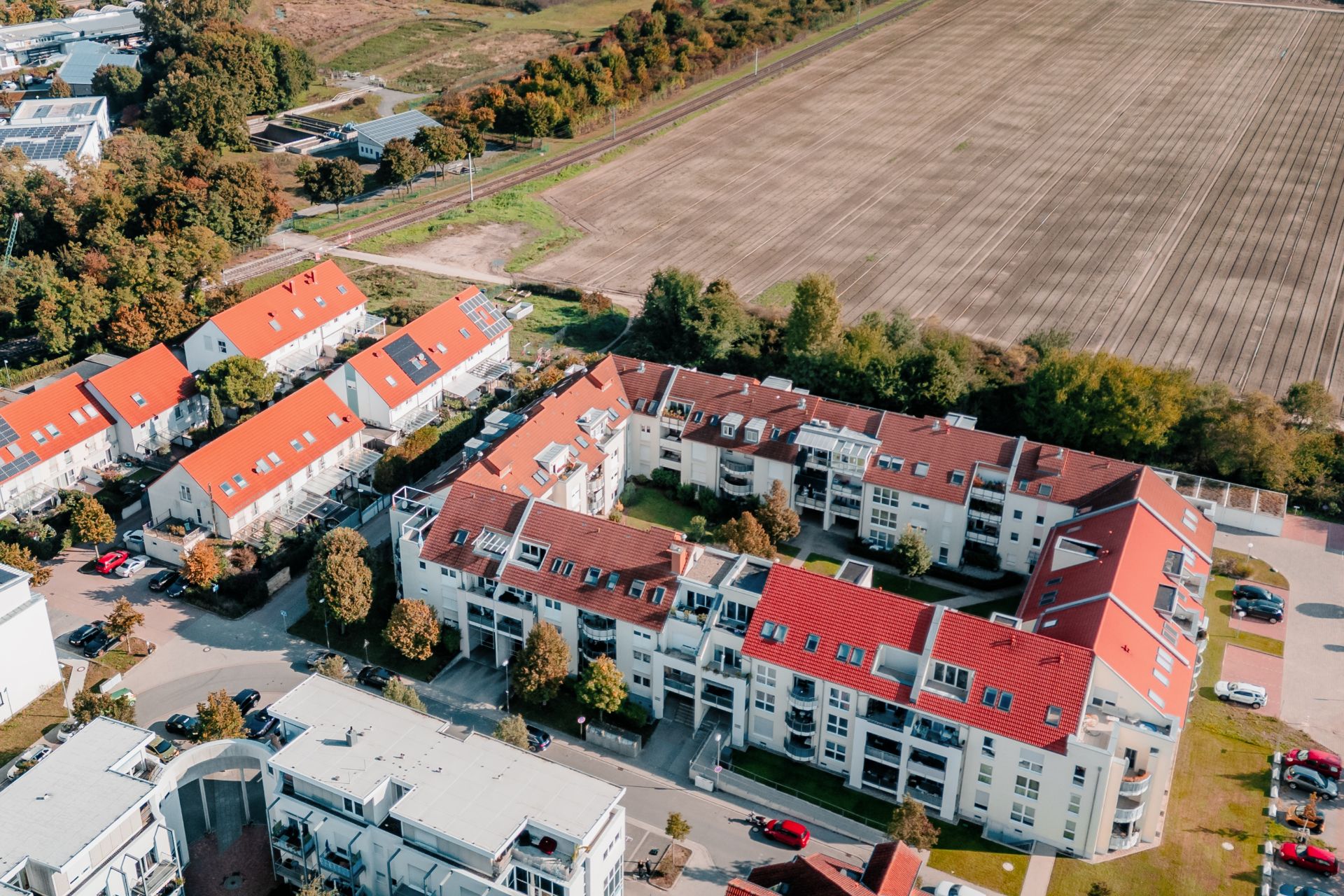 Luftaufnahme von Wohngebäuden mit roten Dächern neben einem großen Feld.