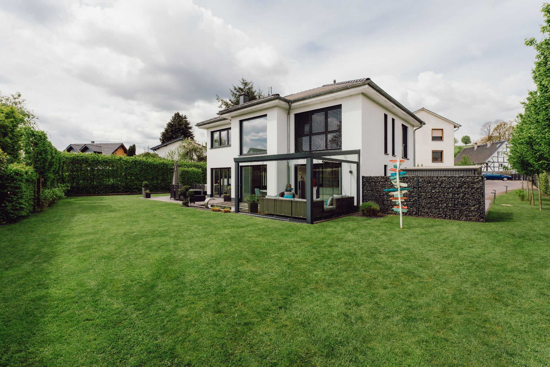 Modernes weißes Wohnhaus mit Wintergarten und großem, gepflegtem Garten.
