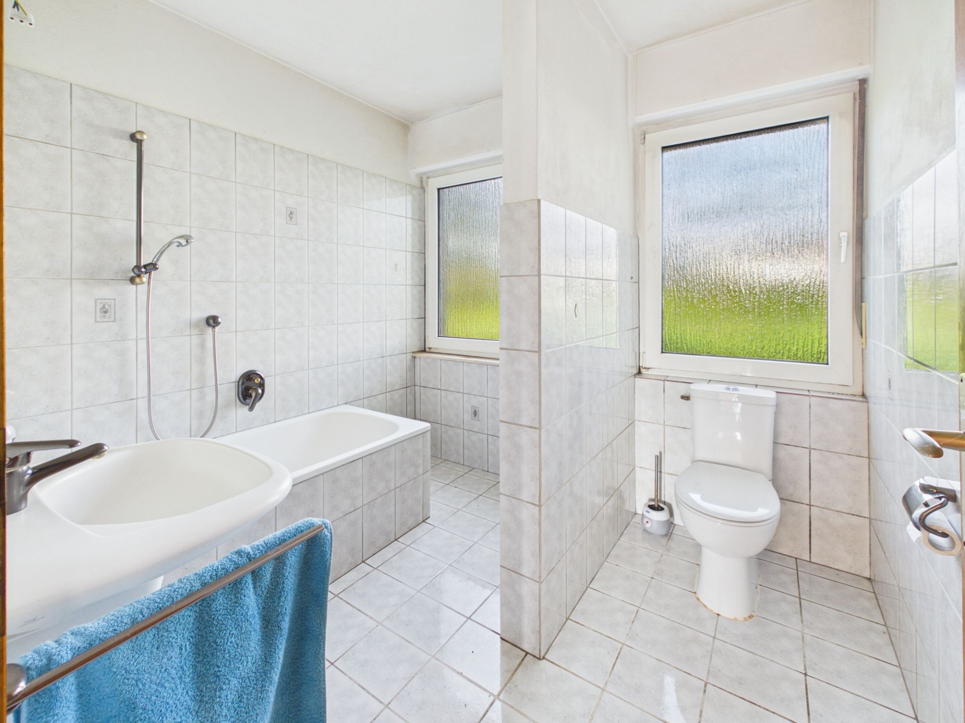 Gefliestes Badezimmer mit Badewanne, Waschbecken und Toilette mit Fenster.