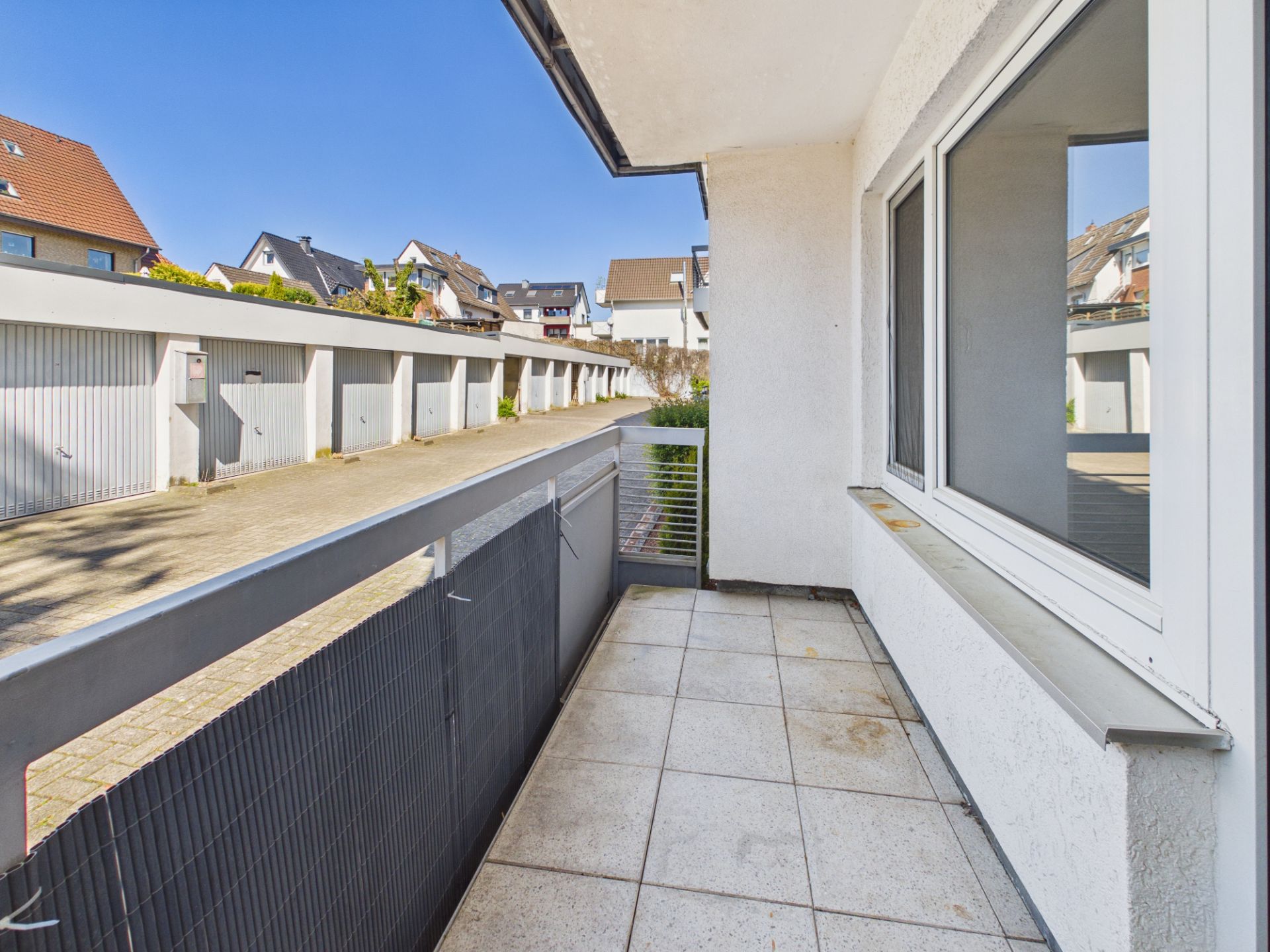Balkon mit Fensterblick auf Garagen und Wohnhäuser an einem sonnigen Tag.