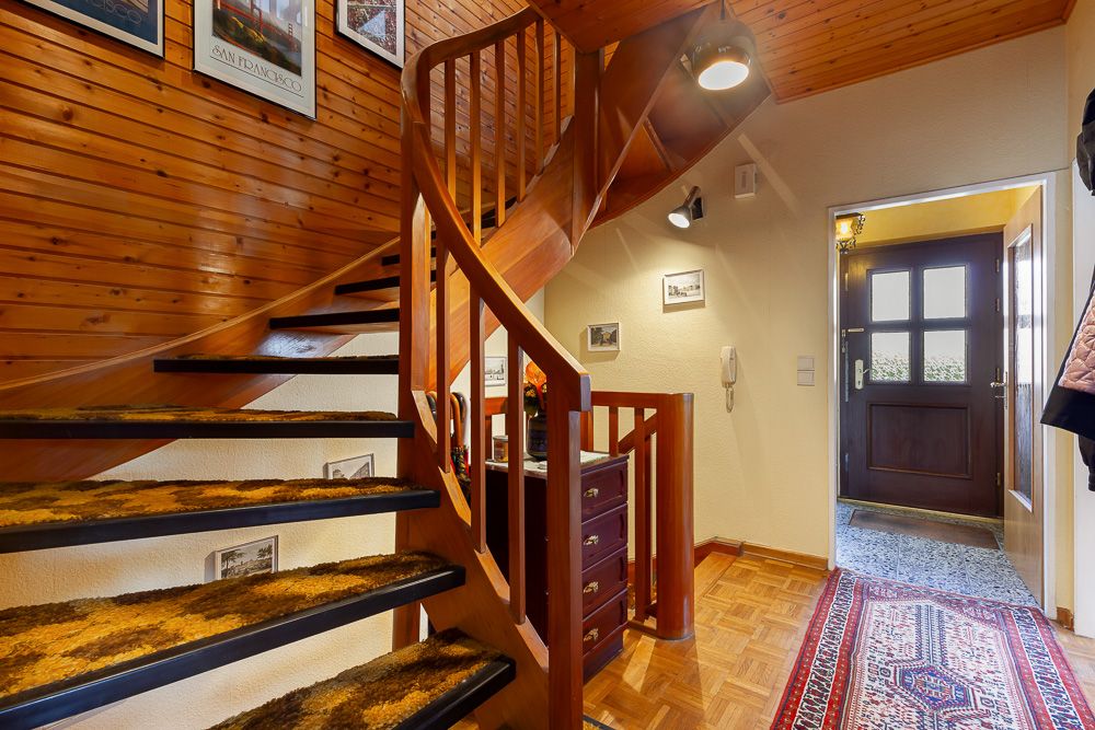 Holztreppe und Flur mit Teppich, Kommode und Eingangstür in einem Wohnhaus.
