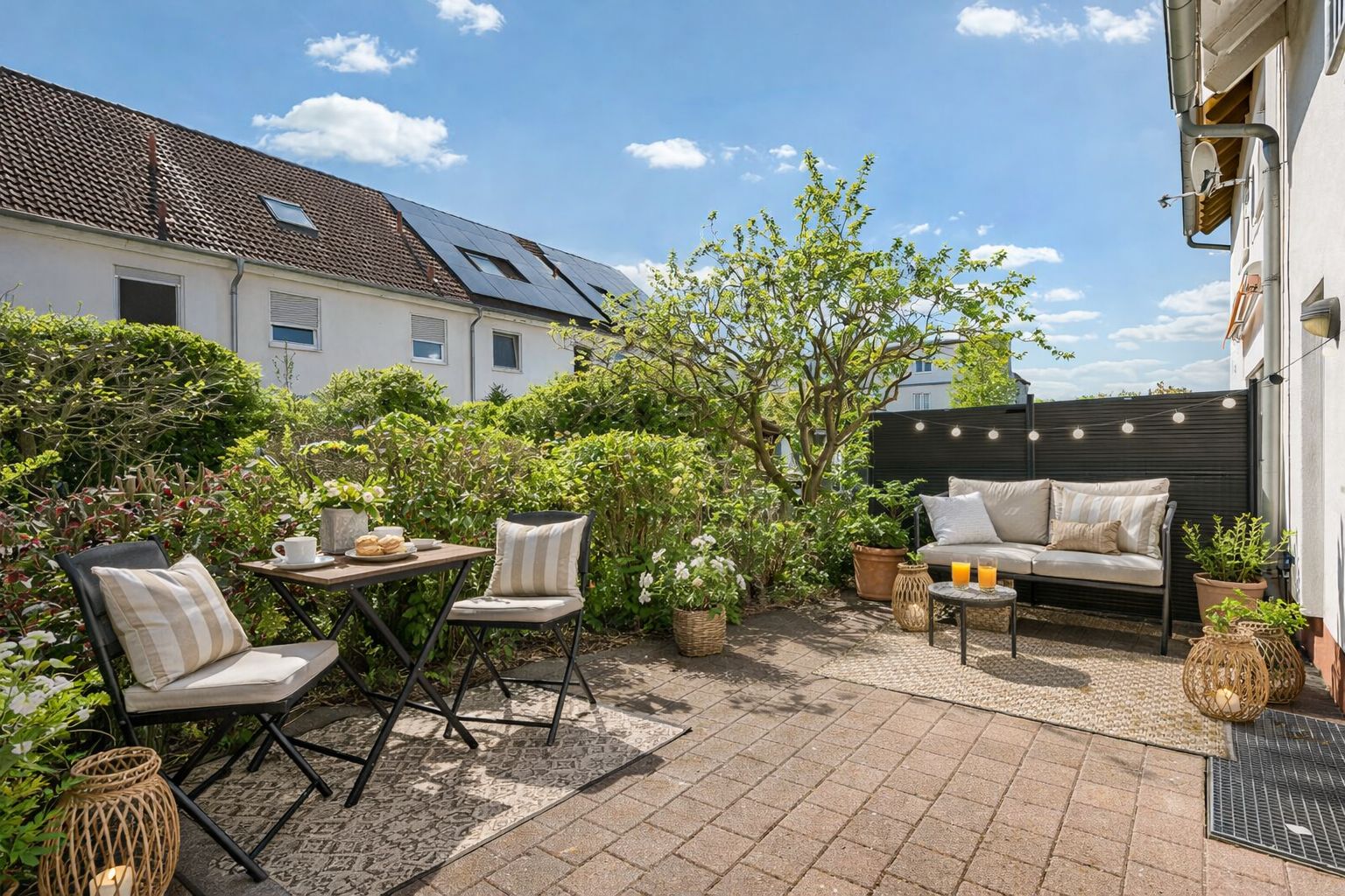 Gepflegte Terrasse mit Sitzmöbeln, Pflanzen und Gartenblick bei sonnigem Wetter.