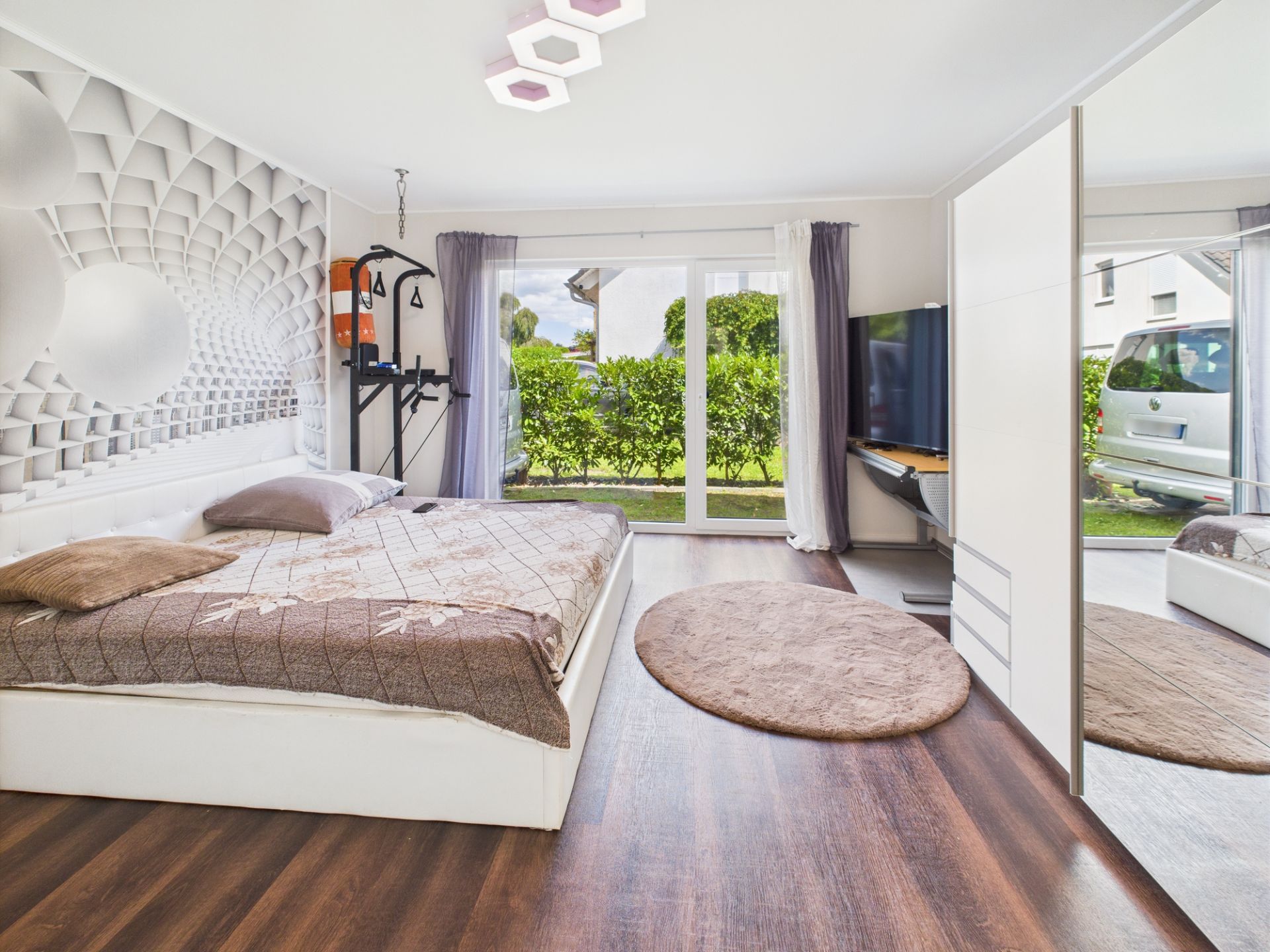 Modernes Schlafzimmer mit großem Bett, Spiegel-Schrank, Fernseher und Blick in den Garten.