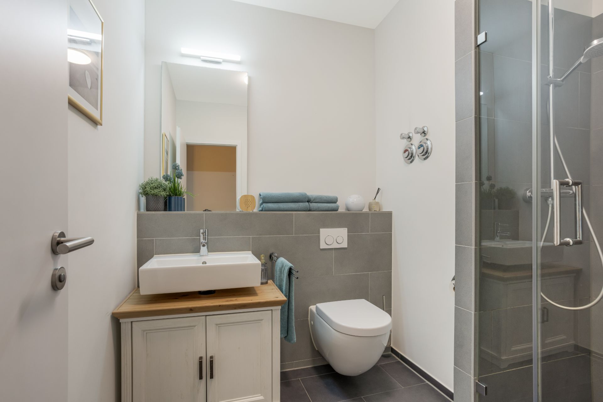 Modernes Badezimmer mit Waschbecken, WC und Glasdusche, dekoriert mit Pflanzen und Handtüchern.