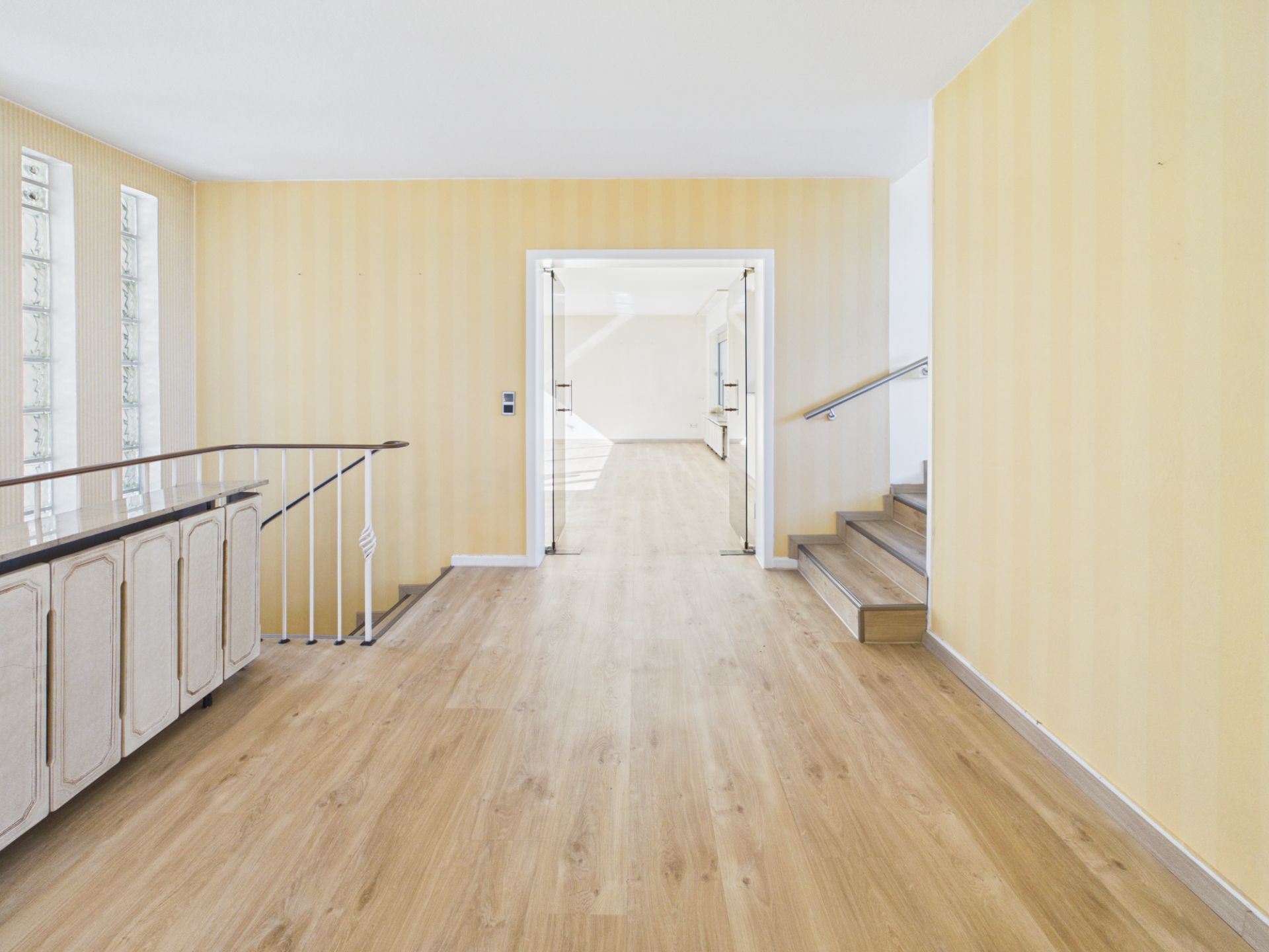 Heller Flur mit Holzfußboden, Geländer, Treppe und Doppeltüren zu einem weiteren Raum.