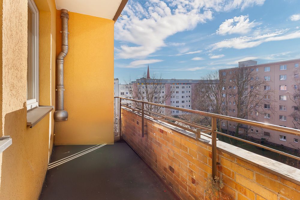 Balkon mit gelber Wand und Blick auf Wohngebäude und blauen Himmel.