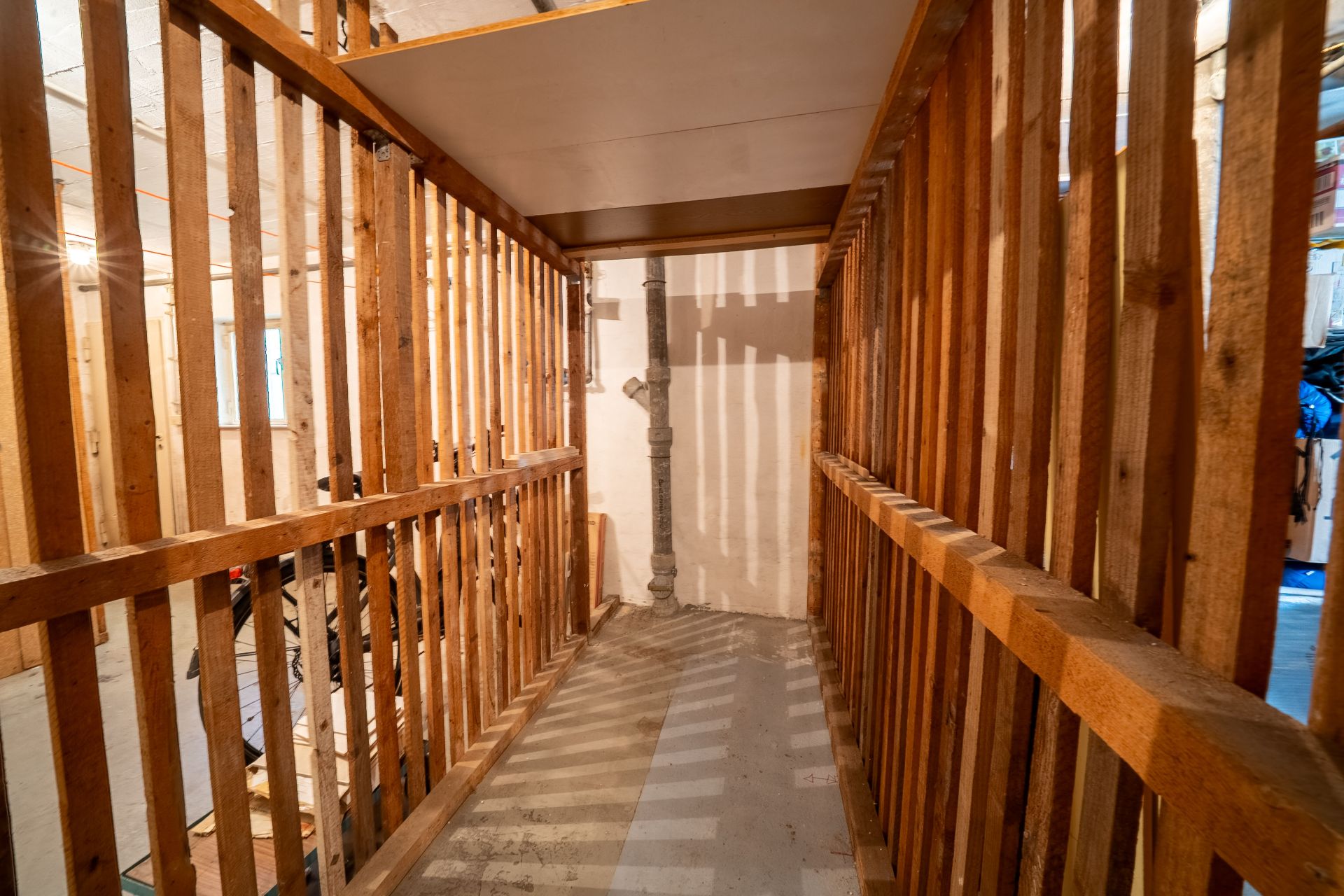 Schmaler Kellerraum mit Holzgitterwänden und Betonboden.