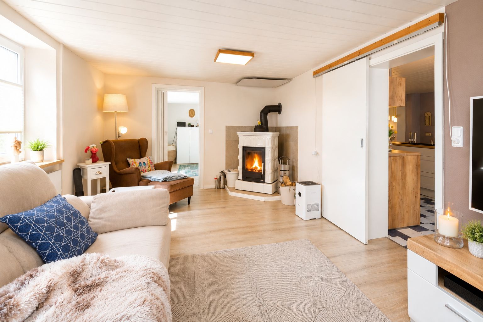 Gemütliches Wohnzimmer mit Sofa, Sessel, Kamin und Zugang zur Küche.