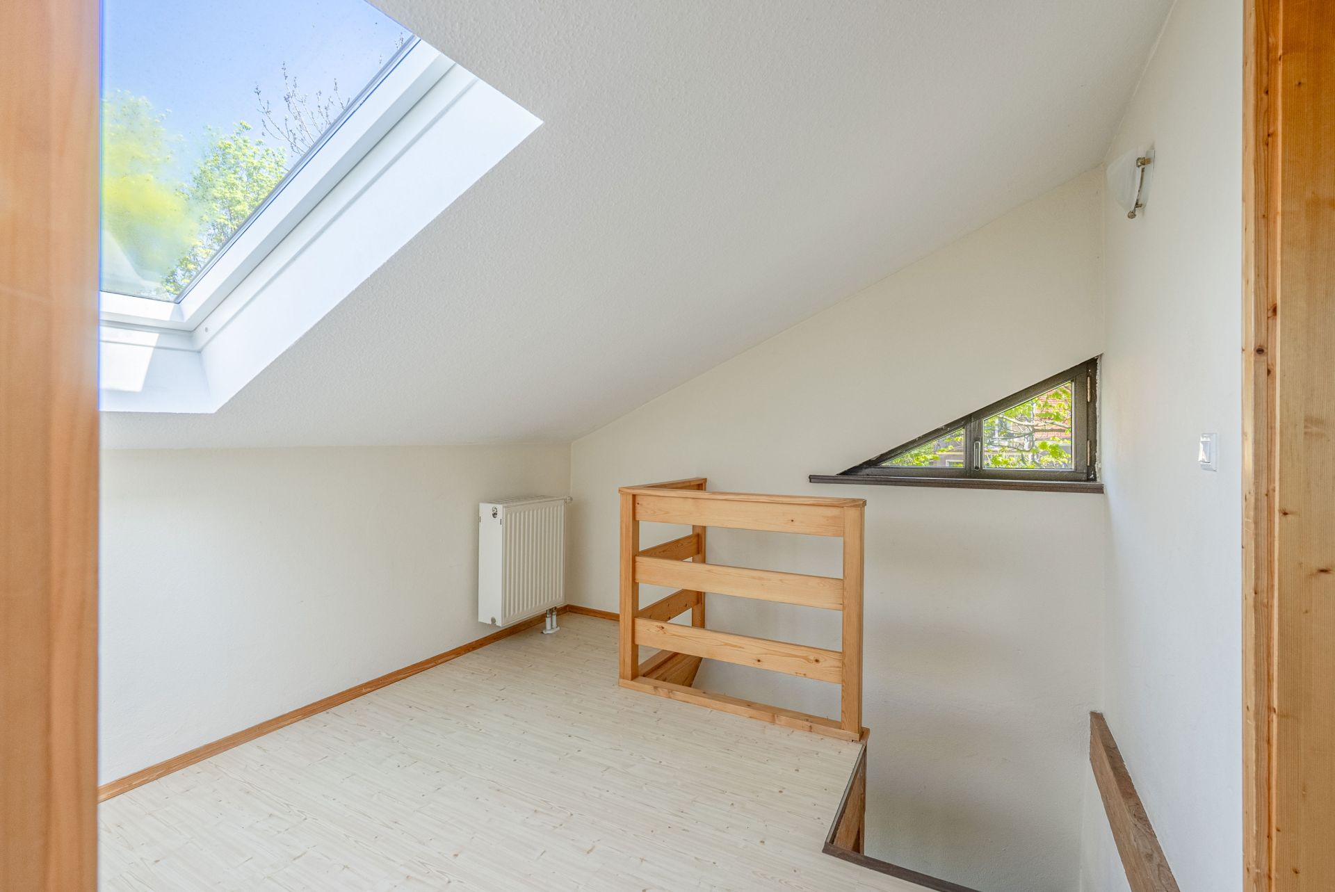 Heller Raum mit Dachfenster, Holzgeländer und Heizung an der Wand.