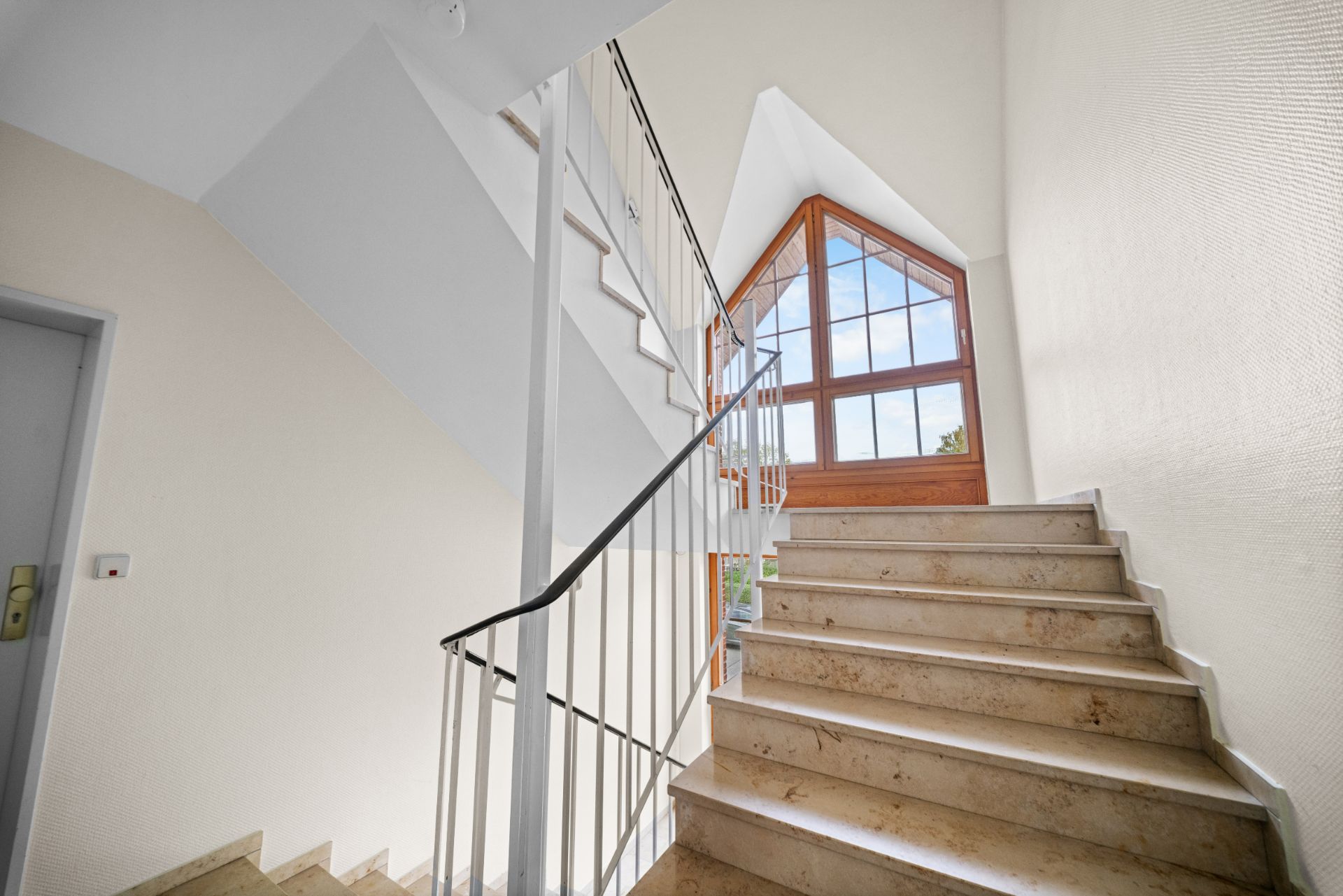 Helles Treppenhaus mit Geländer und großem Fenster am Ende der Treppe.