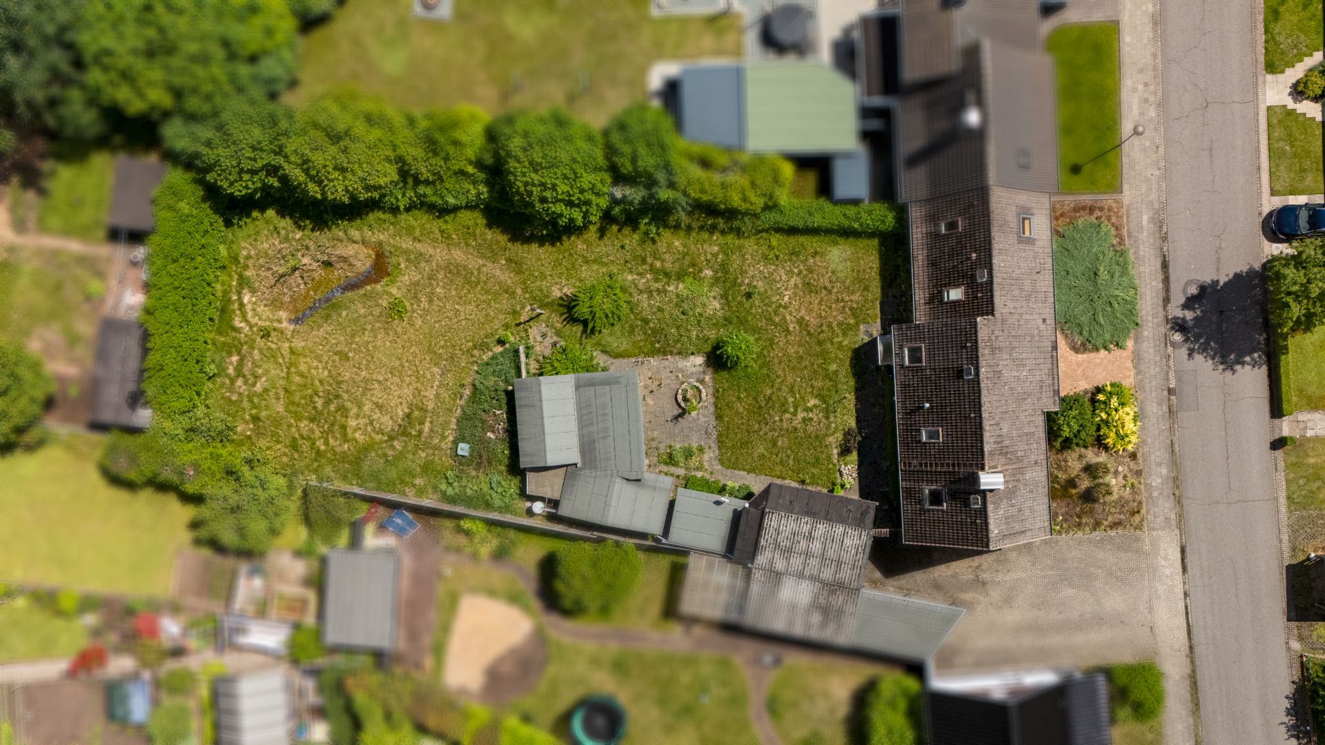 Luftaufnahme eines Wohnhauses mit Garten, Nebengebäuden und angrenzender Straße.