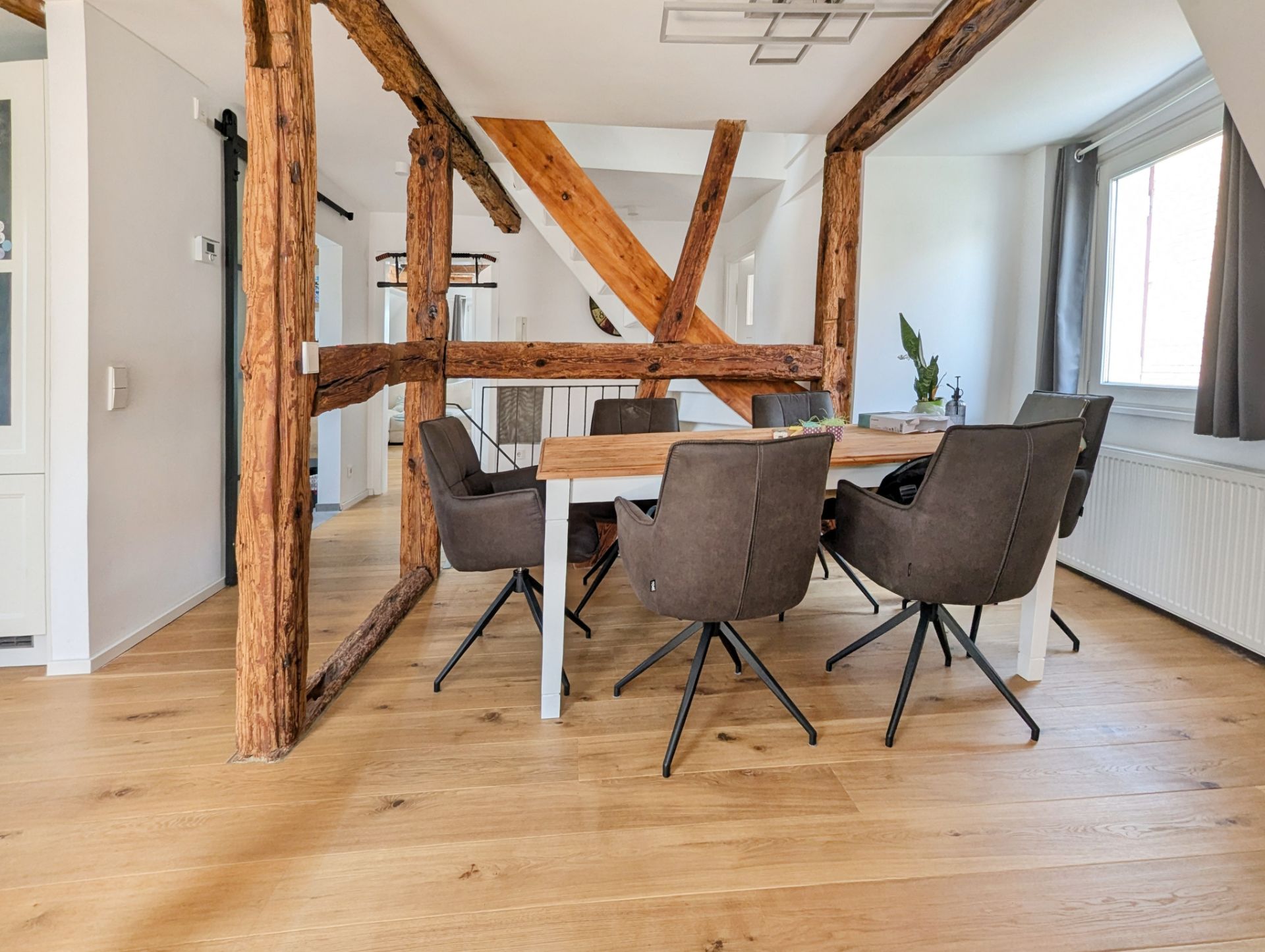 Essbereich mit Holztisch, sechs Stühlen und sichtbaren Holzbalken auf hellem Holzboden.