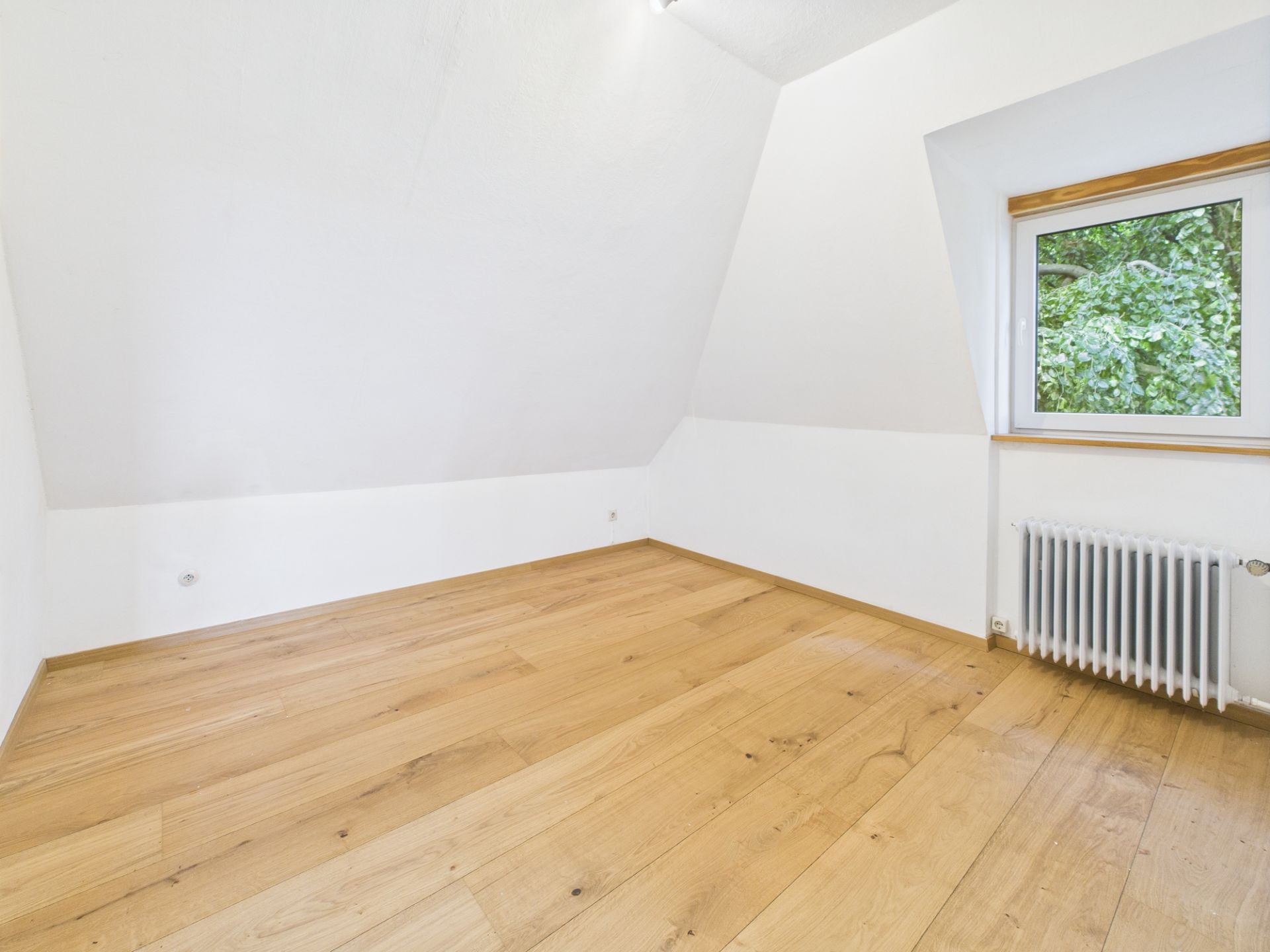 Leerer Raum mit Holzfußboden, weiß gestrichenen Wänden, Fenster und Heizkörper.
