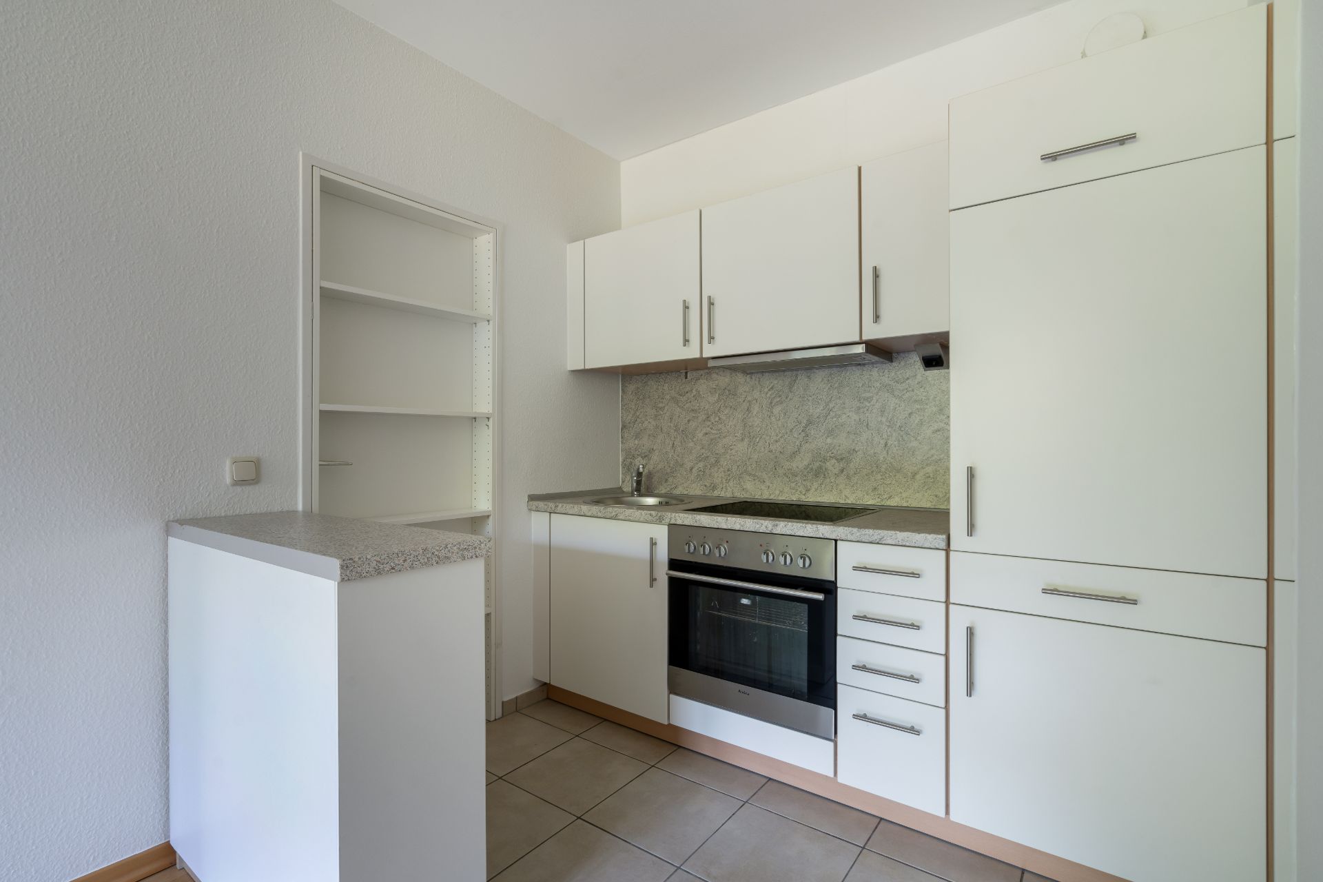 Helle Einbauküche mit weißen Schränken, Herd, Backofen und offenem Regal.