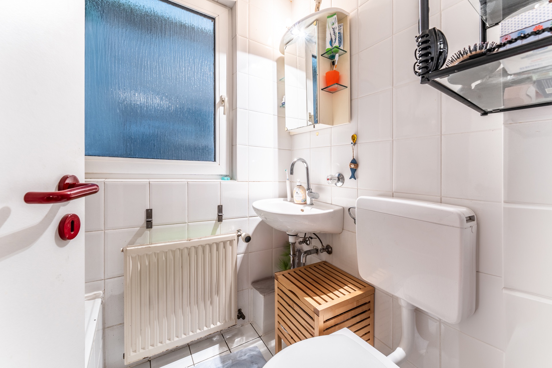 Kleines Badezimmer mit Waschbecken, Toilette, Fenster und Spiegel über dem Waschbecken.