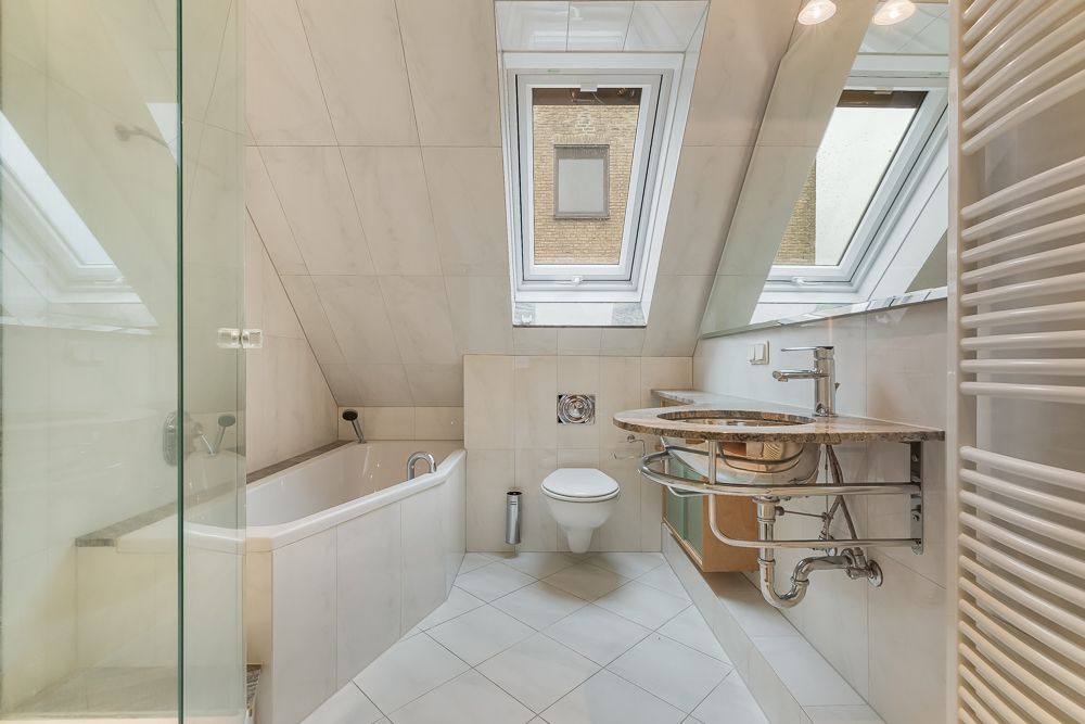 Modernes Bad mit Dachschrägen, Badewanne, Wandtoilette, Waschbecken und großen Dachfenstern.