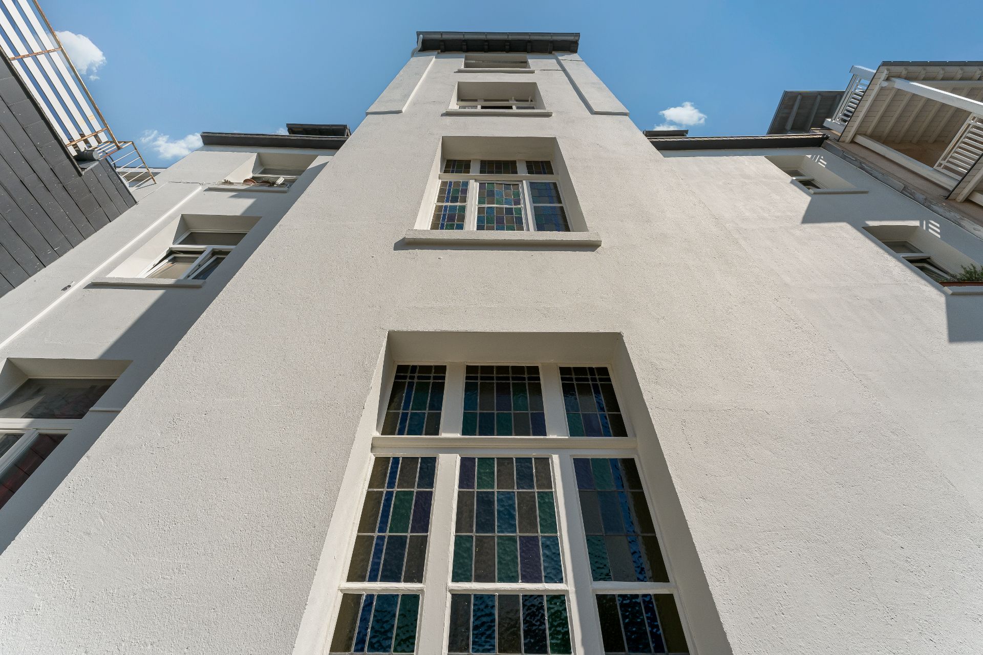 Fassade eines Wohngebäudes mit großen Fenstern und Buntglas, von unten fotografiert.