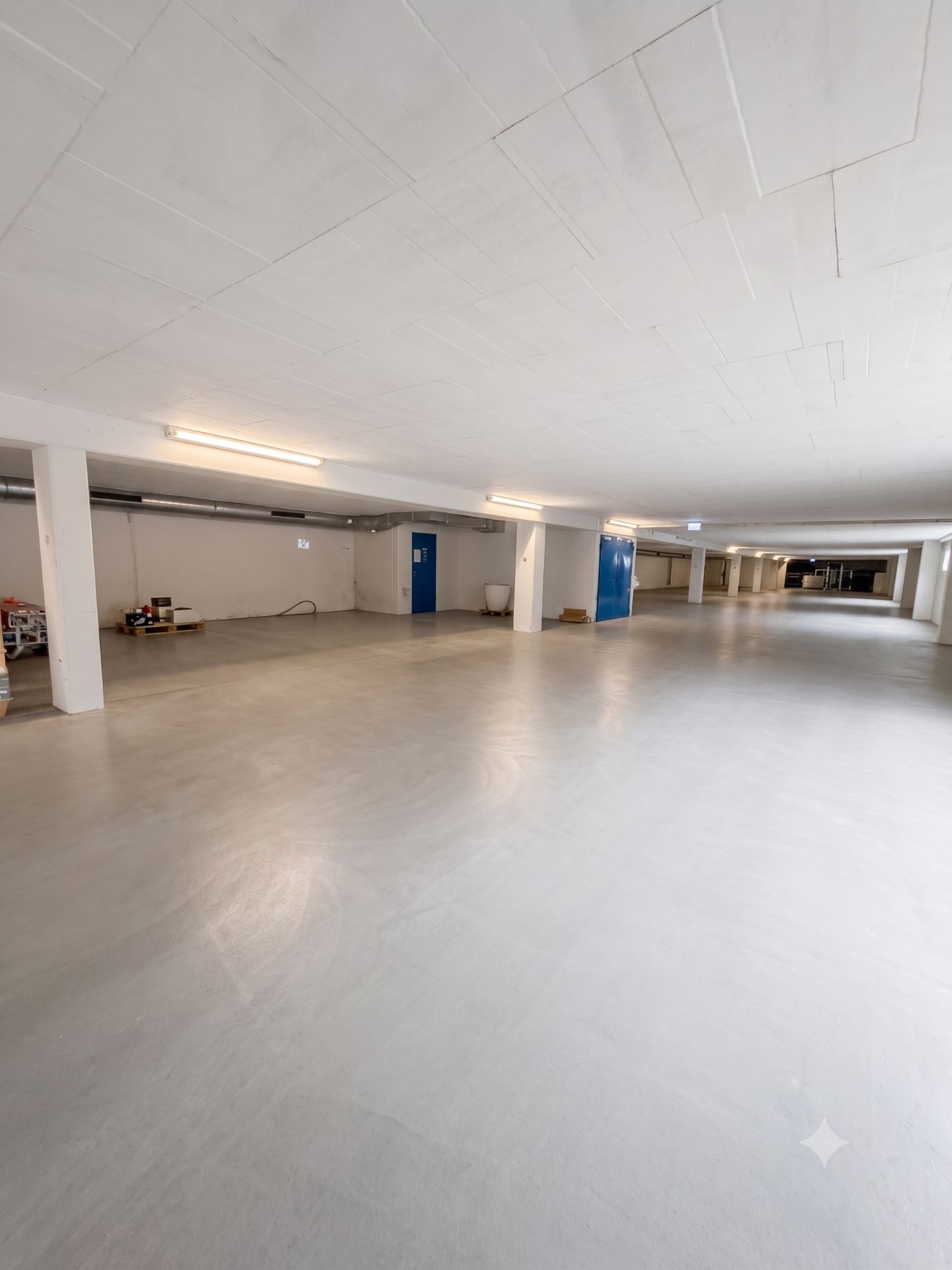 Große, leere Tiefgarage mit weißen Wänden und blauen Türen.