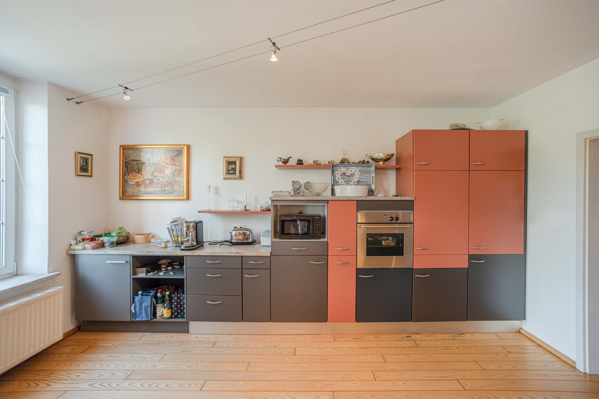 Moderne Einbauküche mit roten und grauen Schränken, Geräten und Bildern an der Wand.