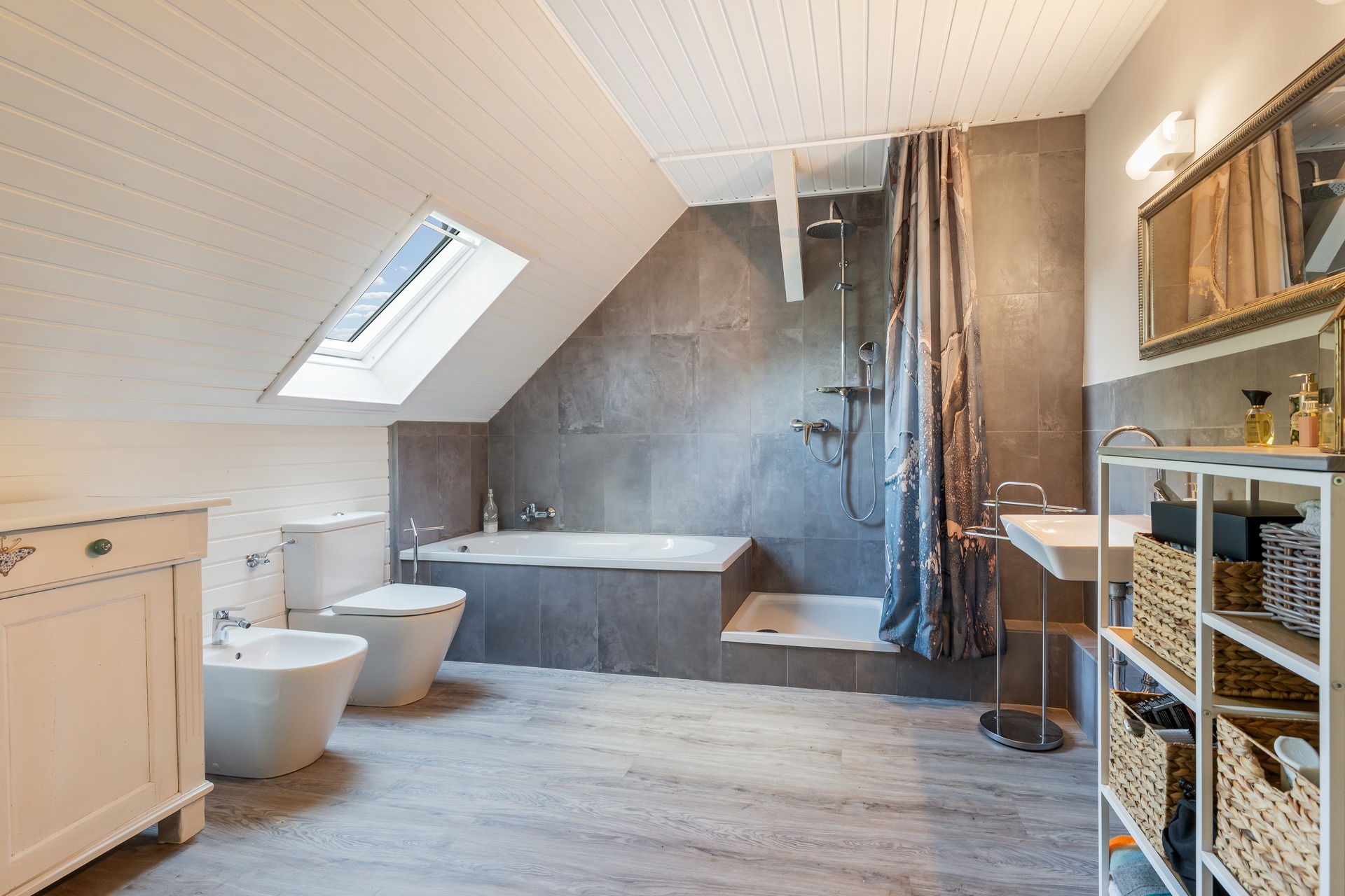 Modernes Badezimmer mit Badewanne, Dusche, WC, Bidet und Waschbecken unter einer Dachschräge.