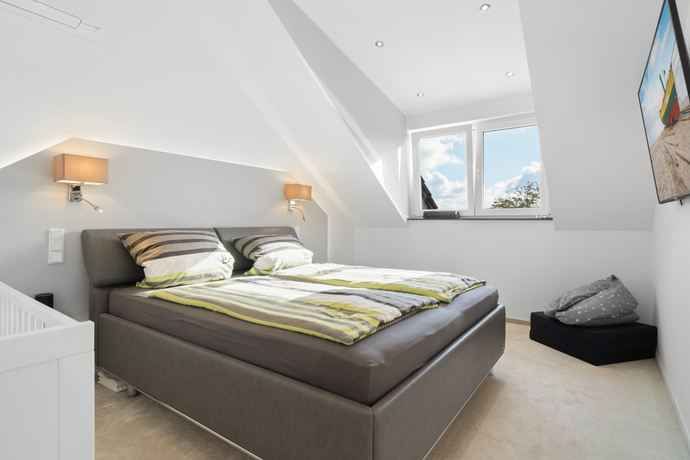 Modernes Schlafzimmer mit Doppelbett unter Dachschräge, zwei Fenstern und Wandlampen.