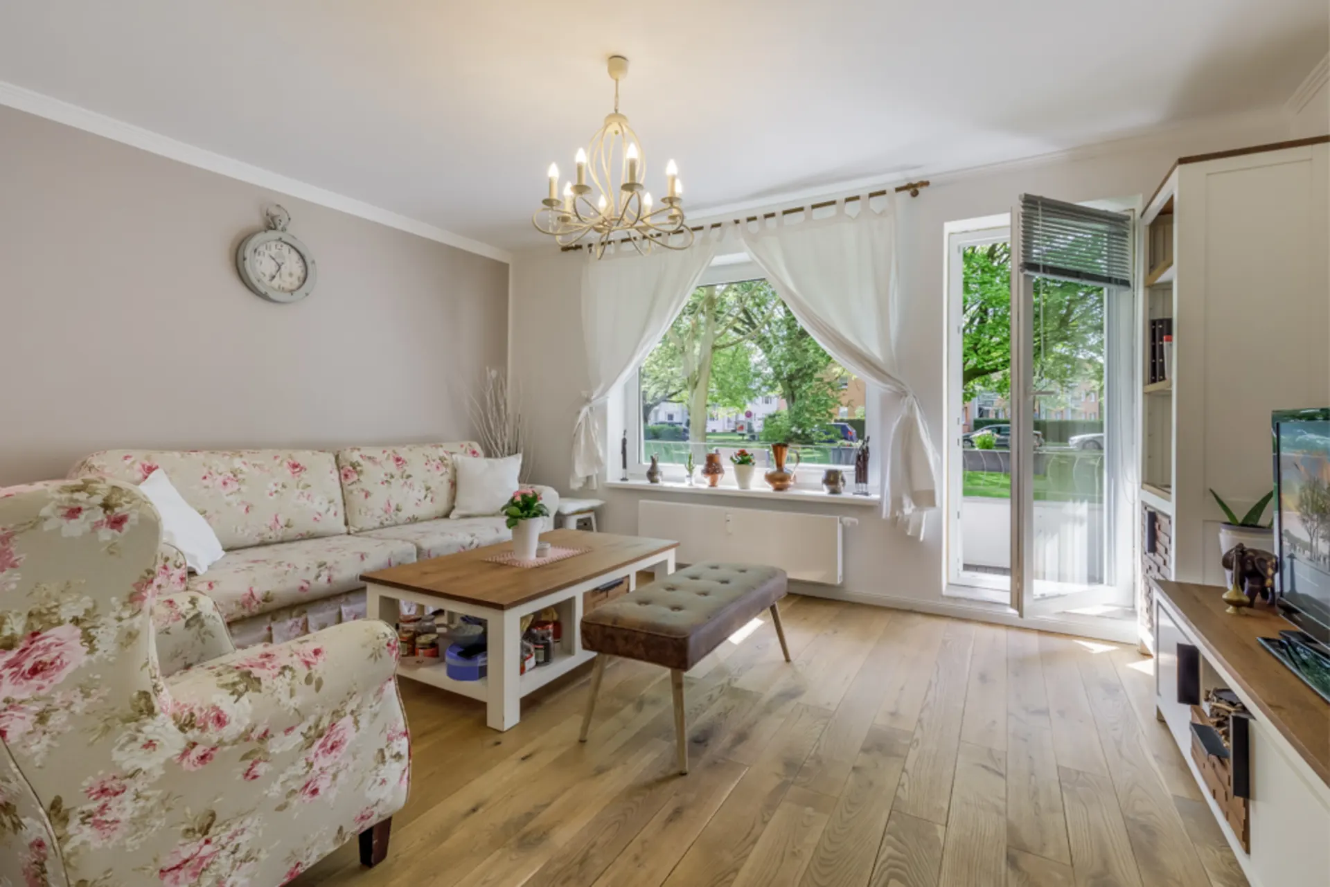 Helles Wohnzimmer mit Blumenmuster-Sofa, Couchtisch und offener Tür zum Balkon.