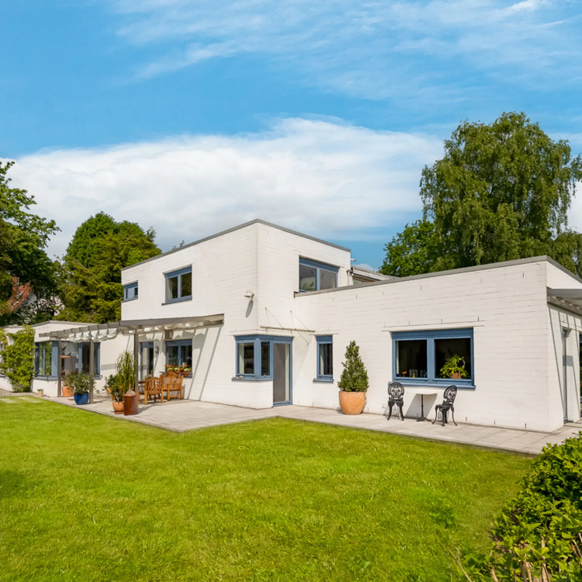 Modernes weißes Wohnhaus mit flachem Dach, großen Fenstern und Terrasse im Garten.
