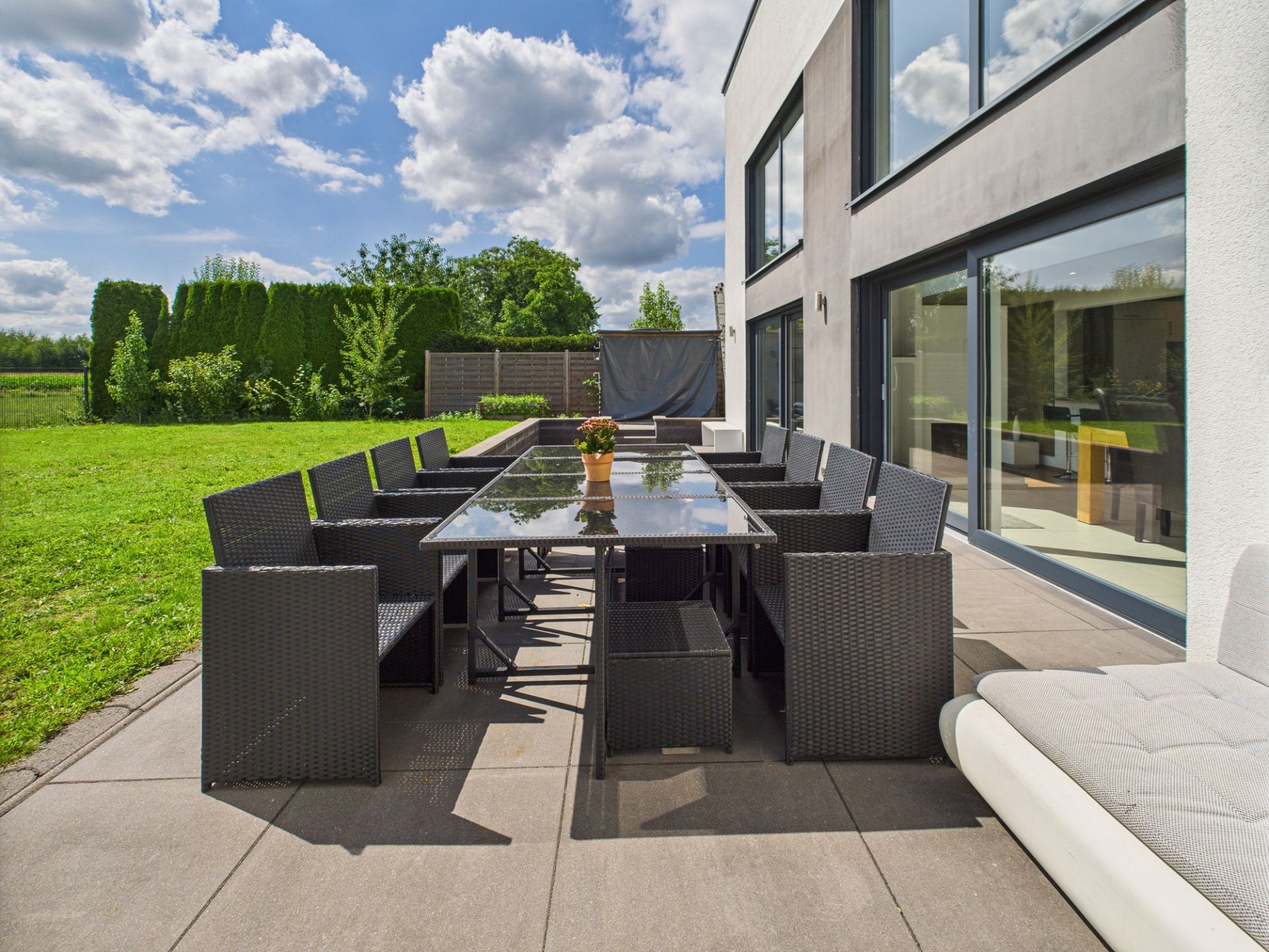 Moderne Terrasse mit großem Esstisch, vielen Stühlen und Blick auf Garten.